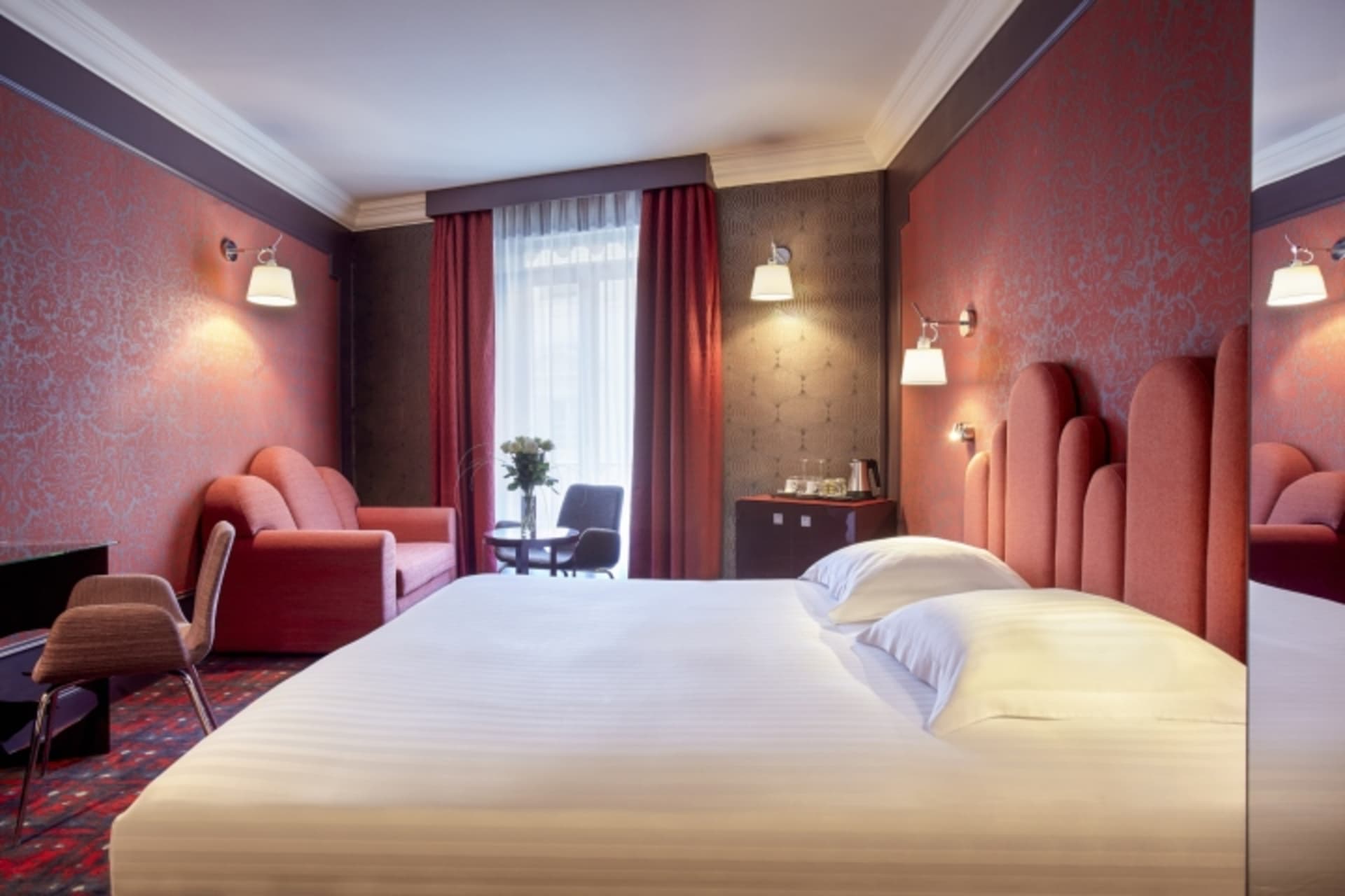 Modern hotel room with a bed, armchair, sofa, and coffee table.