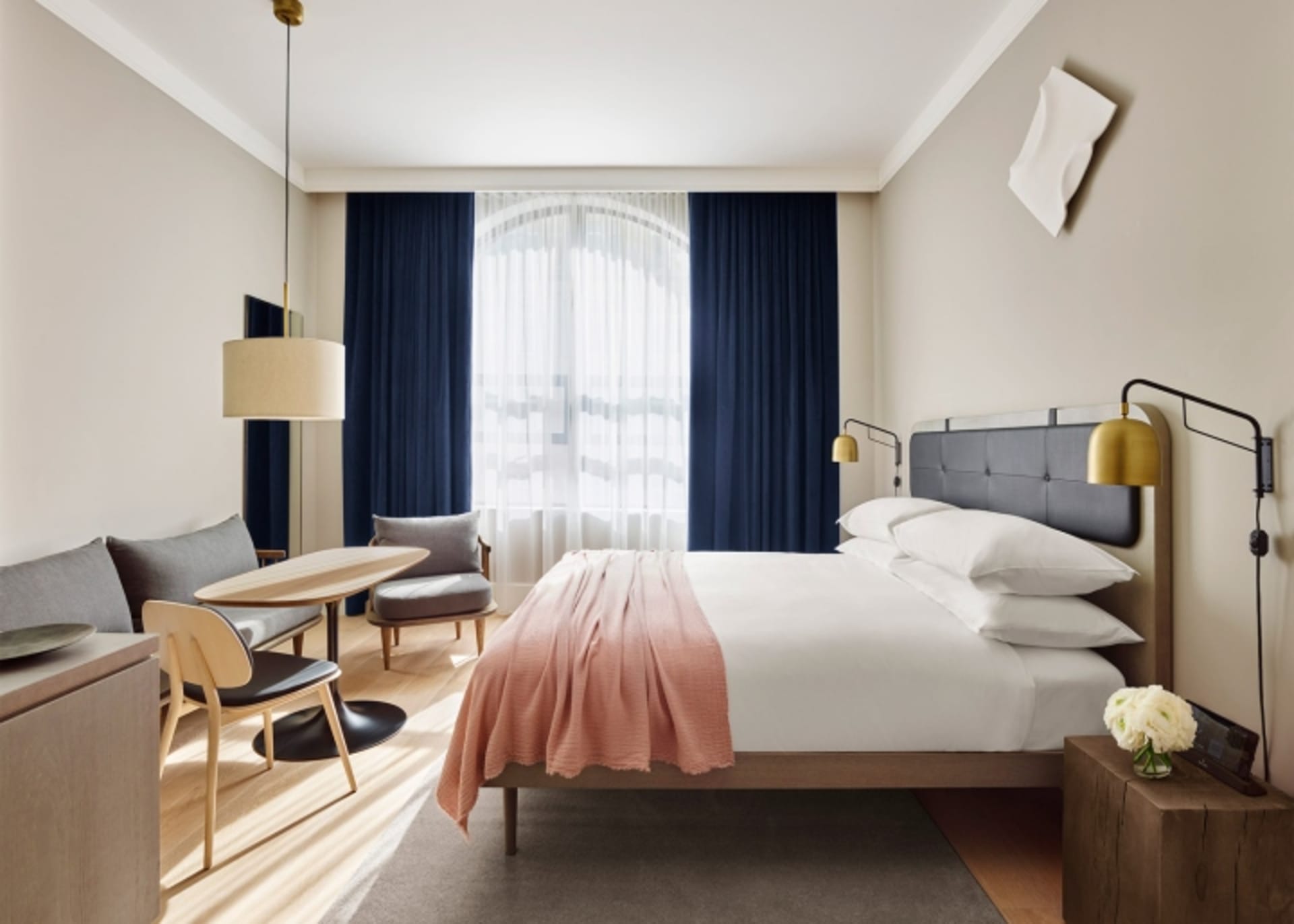 Modern minimalist bedroom with a leather headboard, white bedding, and a wooden floor.