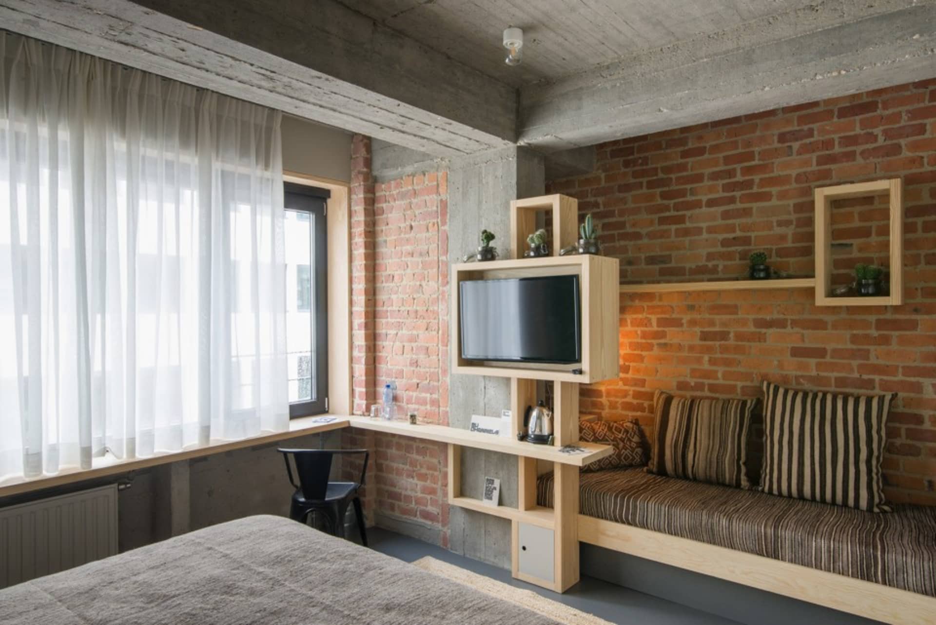 A modern industrial residential space with wooden shelves, brick walls, and concrete flooring.