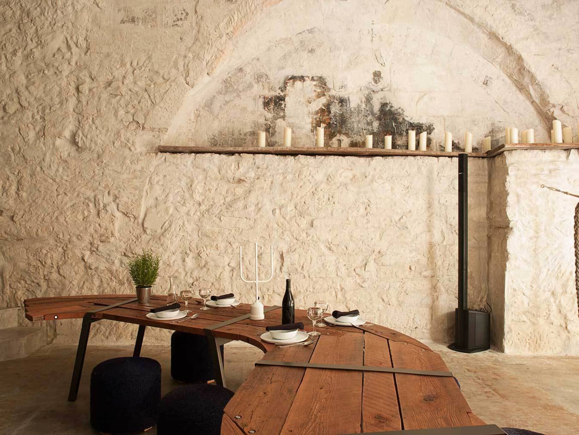 A modern restaurant dining room with a wooden table, white plates, wine glasses, and candles.
