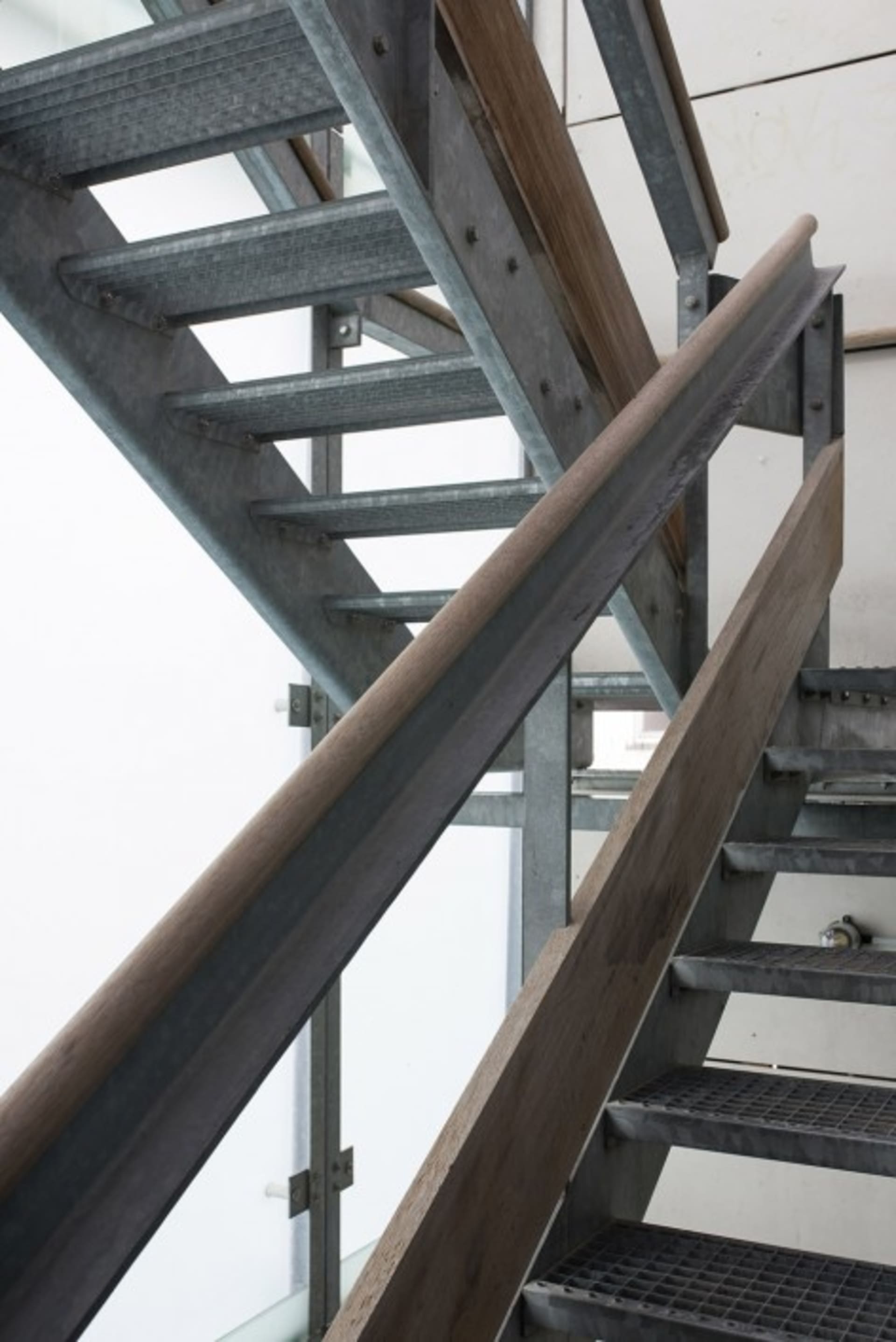 Metallic stairs leading upwards with wood railing and handrail.