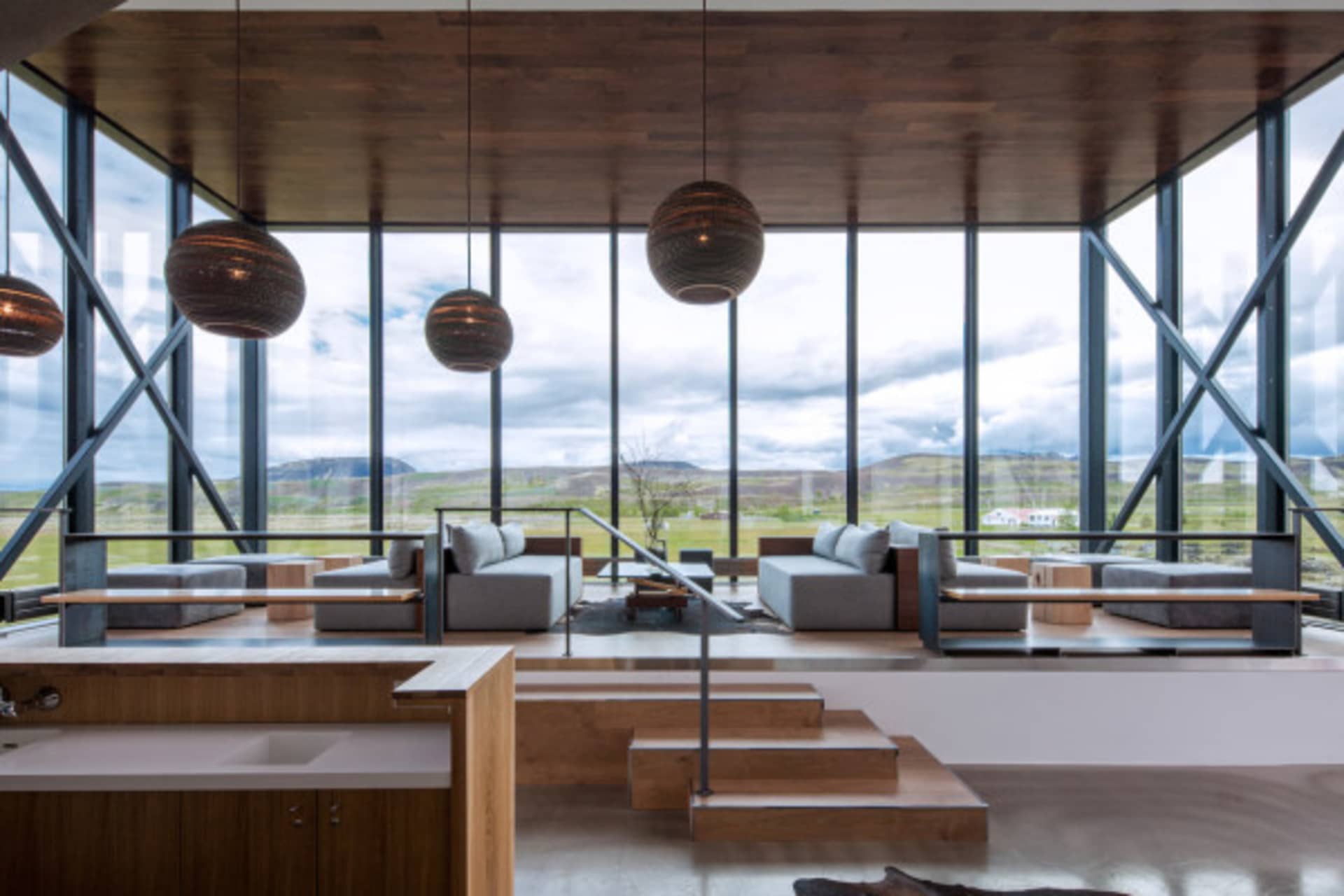 Modern living room featuring large glass windows with a view outside and wooden flooring.