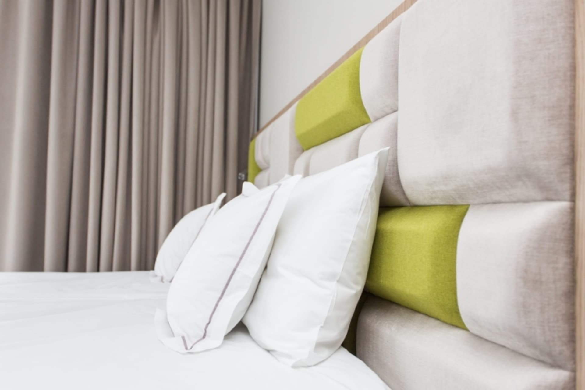 A minimalist bedroom with a fabric headboard featuring green accents and white pillows.