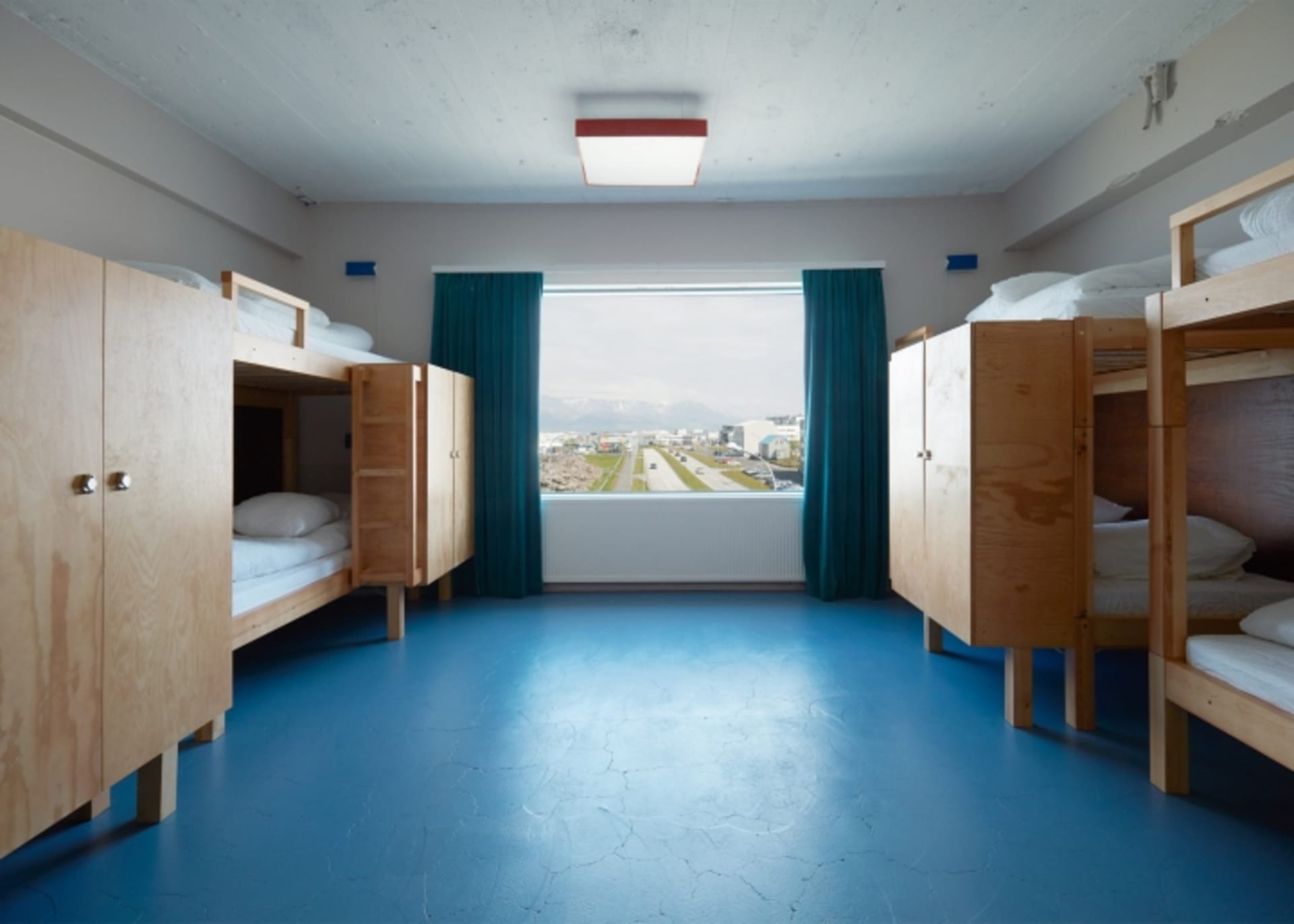 Modern minimalist bedroom featuring wooden bunk beds with view of cityscape through large windows.