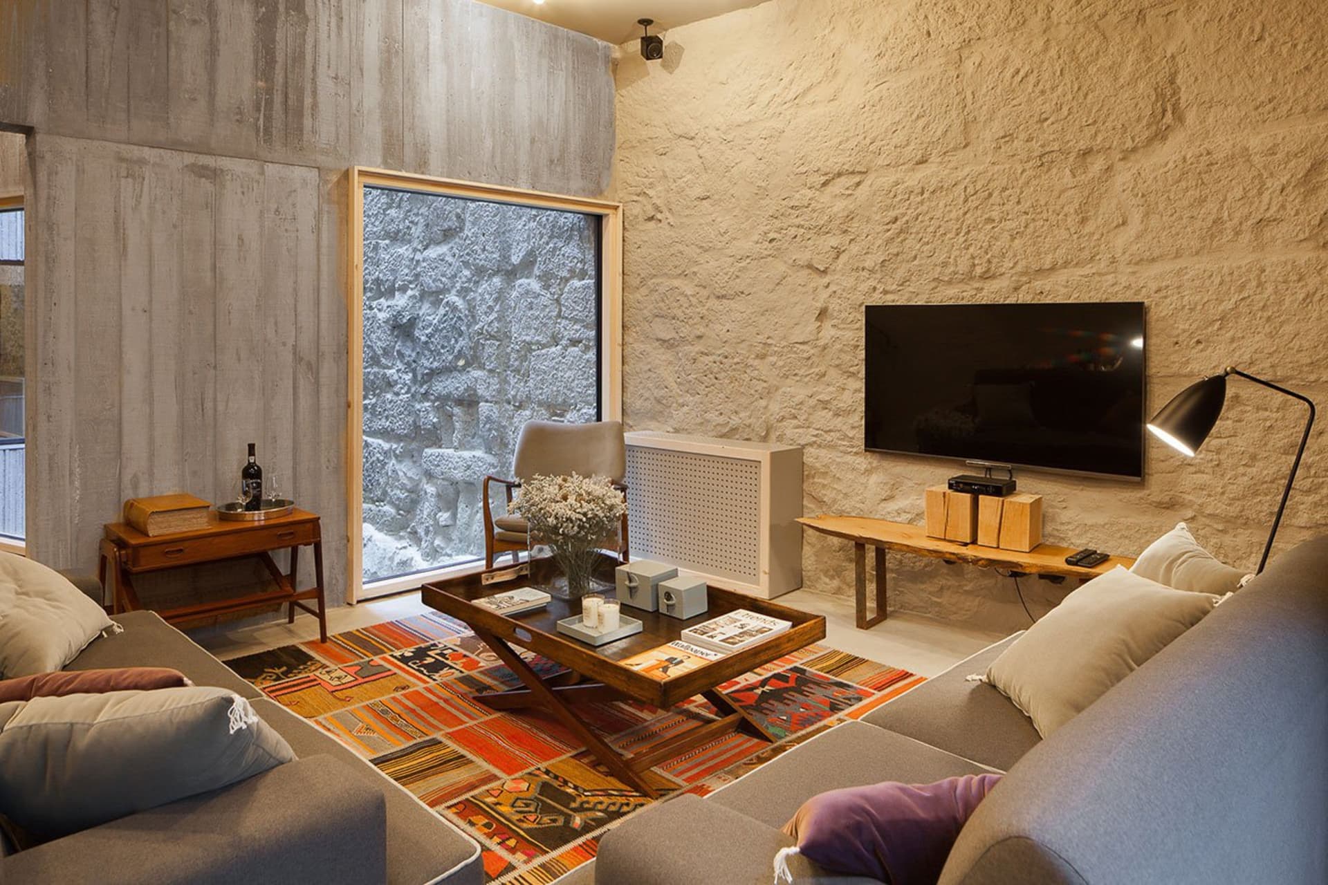 A modern industrial living room with exposed concrete walls, wooden furniture, and a colorful rug.