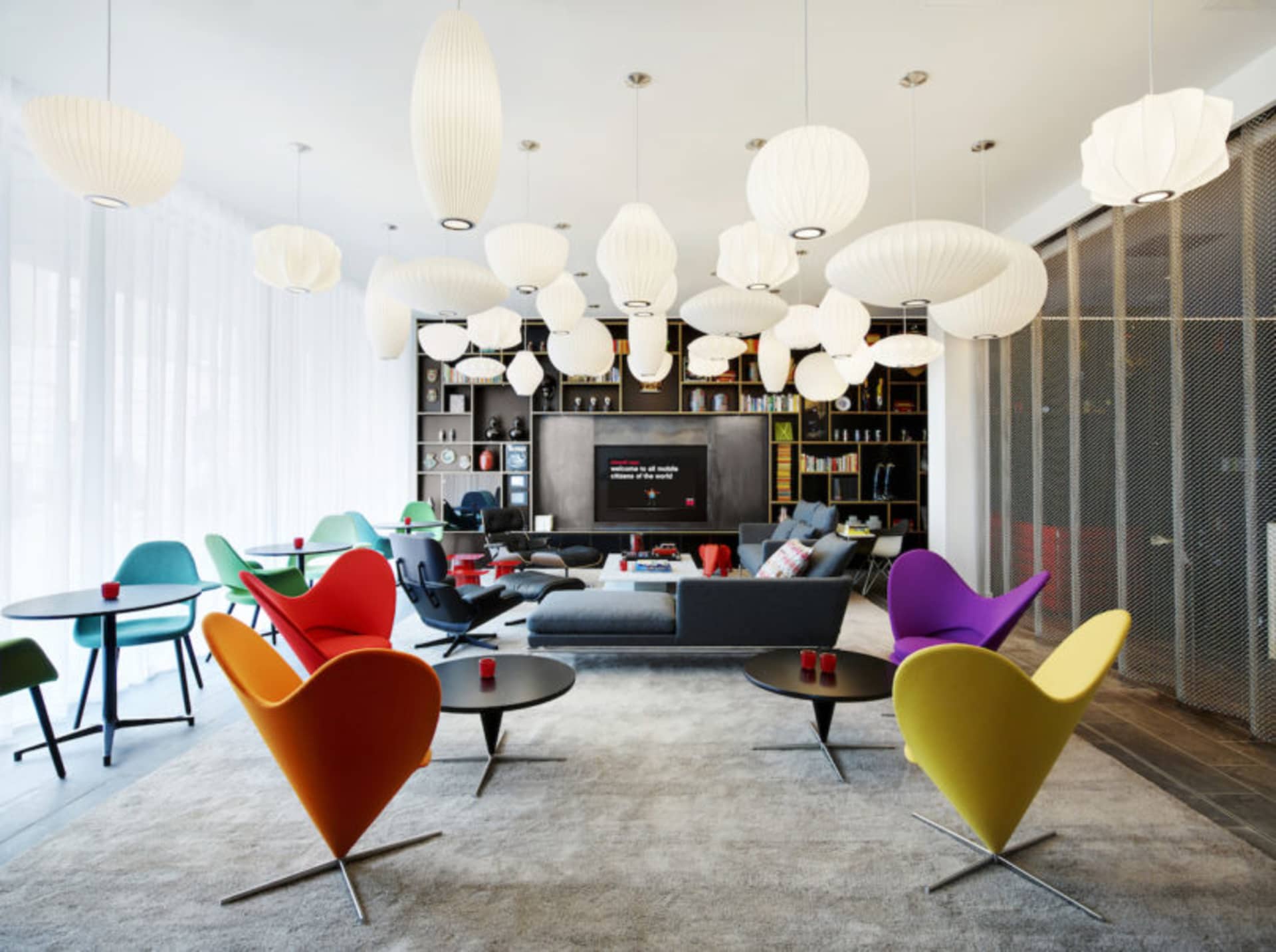 A mid-century modern living room with colorful cone-shaped chairs, a black sofa, and hanging white pendant lights.