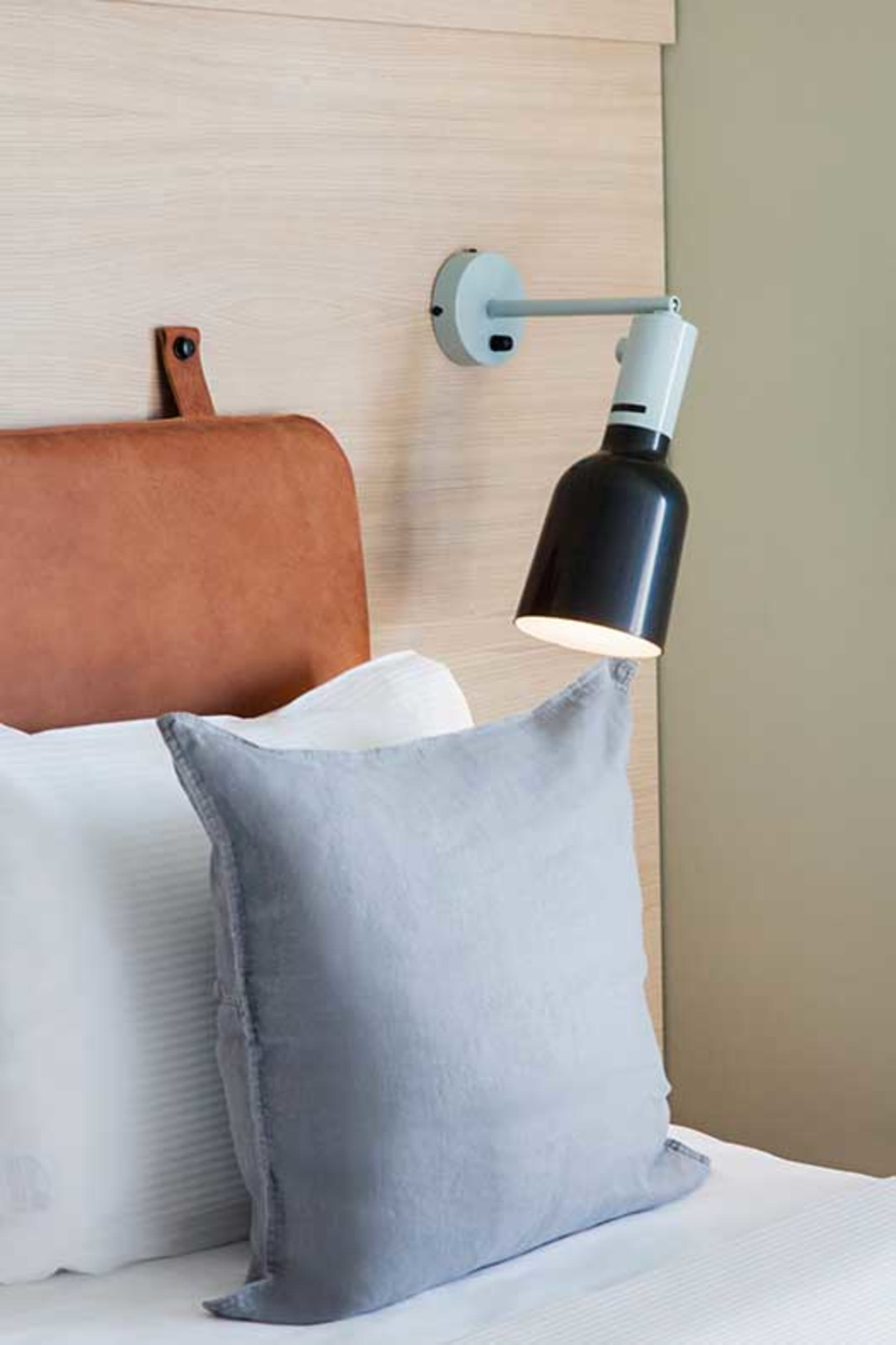 A minimalist bedroom with a gray cushion, a leather headboard, and a modern lamp on the wall.