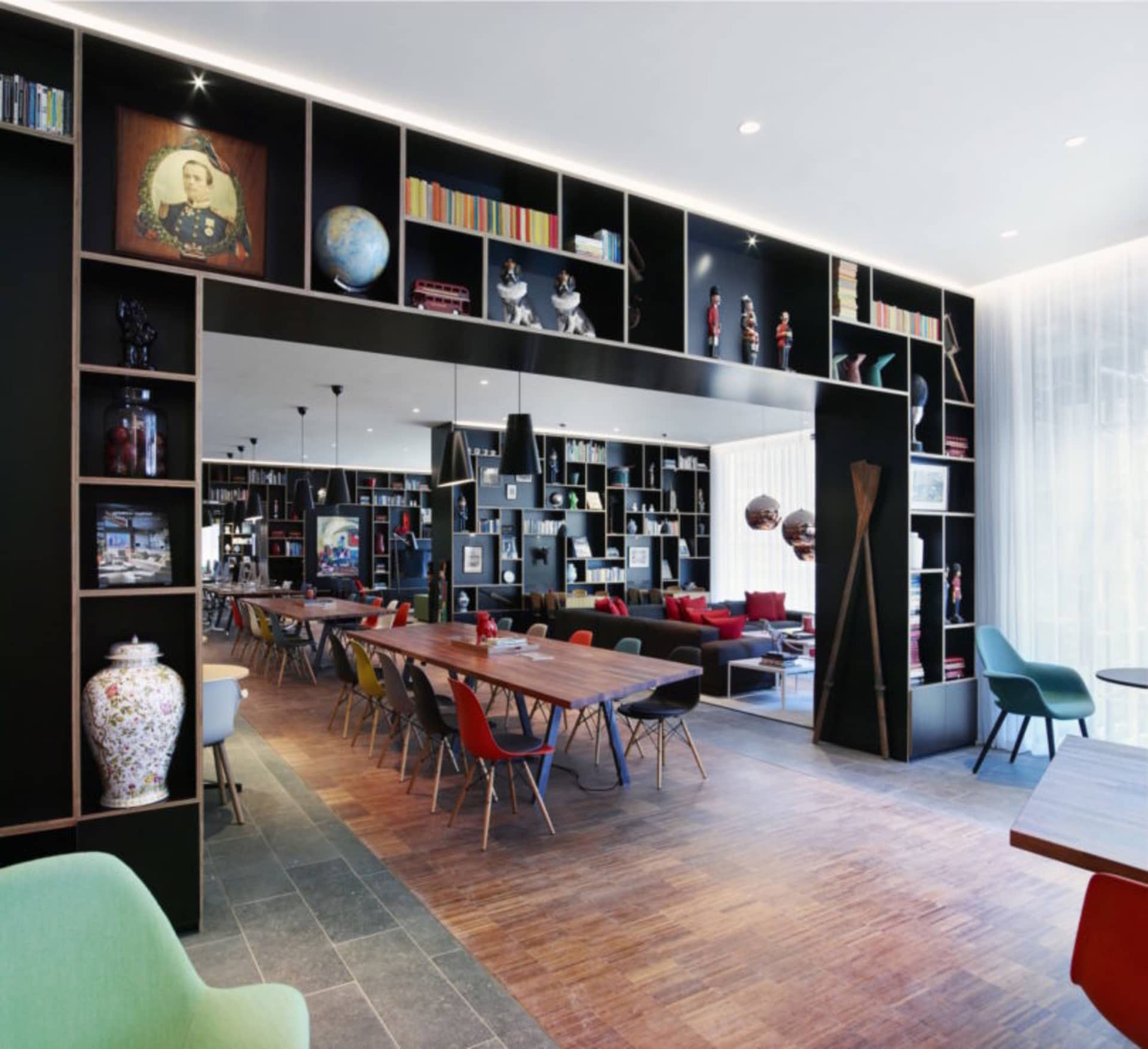 A modern coworking space featuring a combination of wooden furniture, metal accents, and glass elements, with a large bookshe