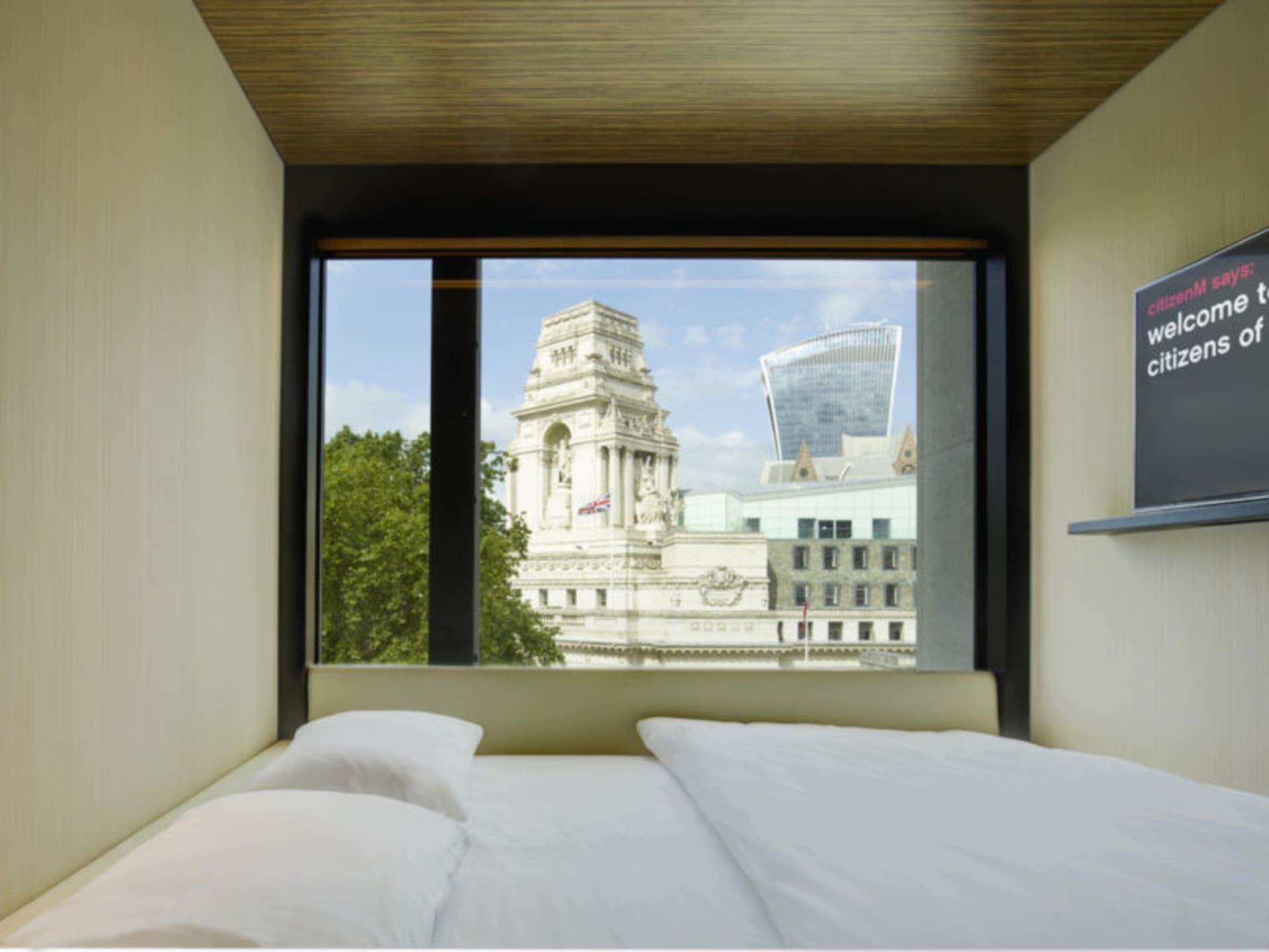 A modern hotel room pod overlooking a historic and modern cityscape through a large glass window.