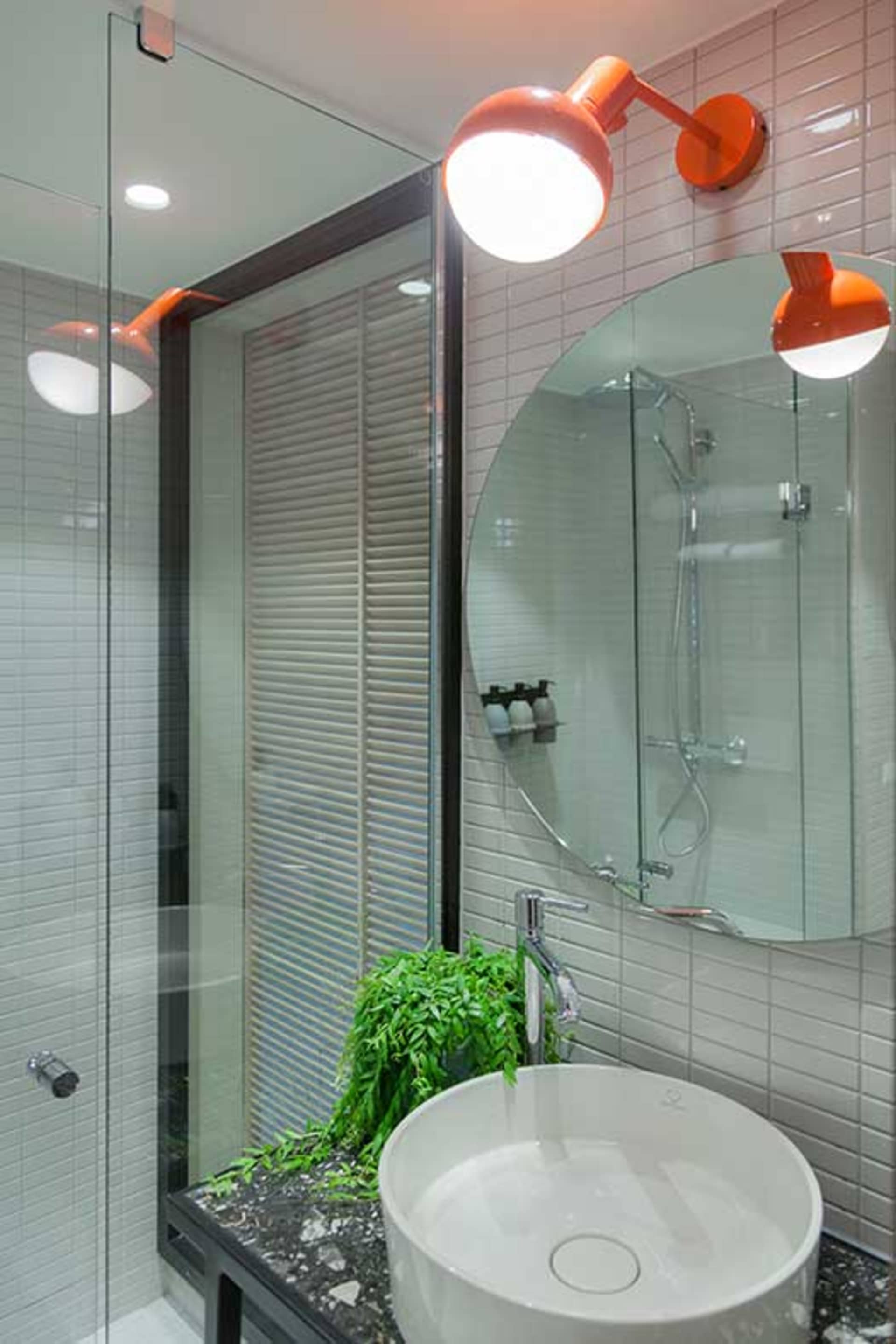 Modern bathroom with concrete and ceramic tiles, round sink, orange lights, and green plant.