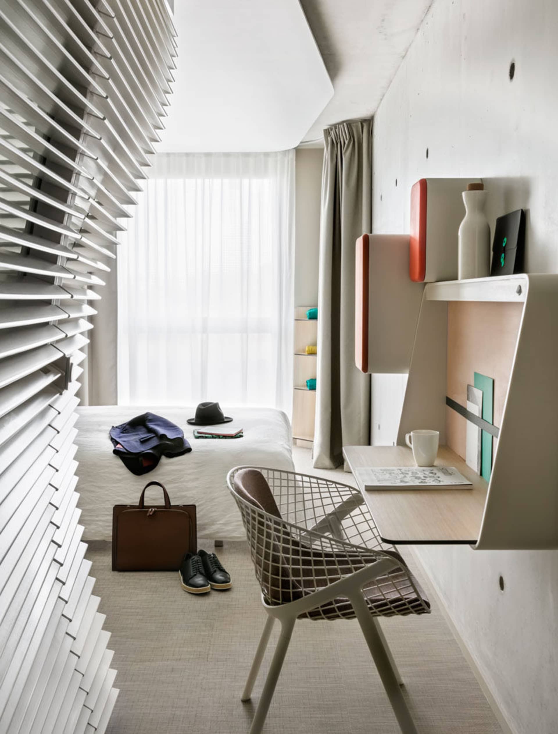 A modern minimalist bedroom with a white bed, metal chair, and minimalist design elements.