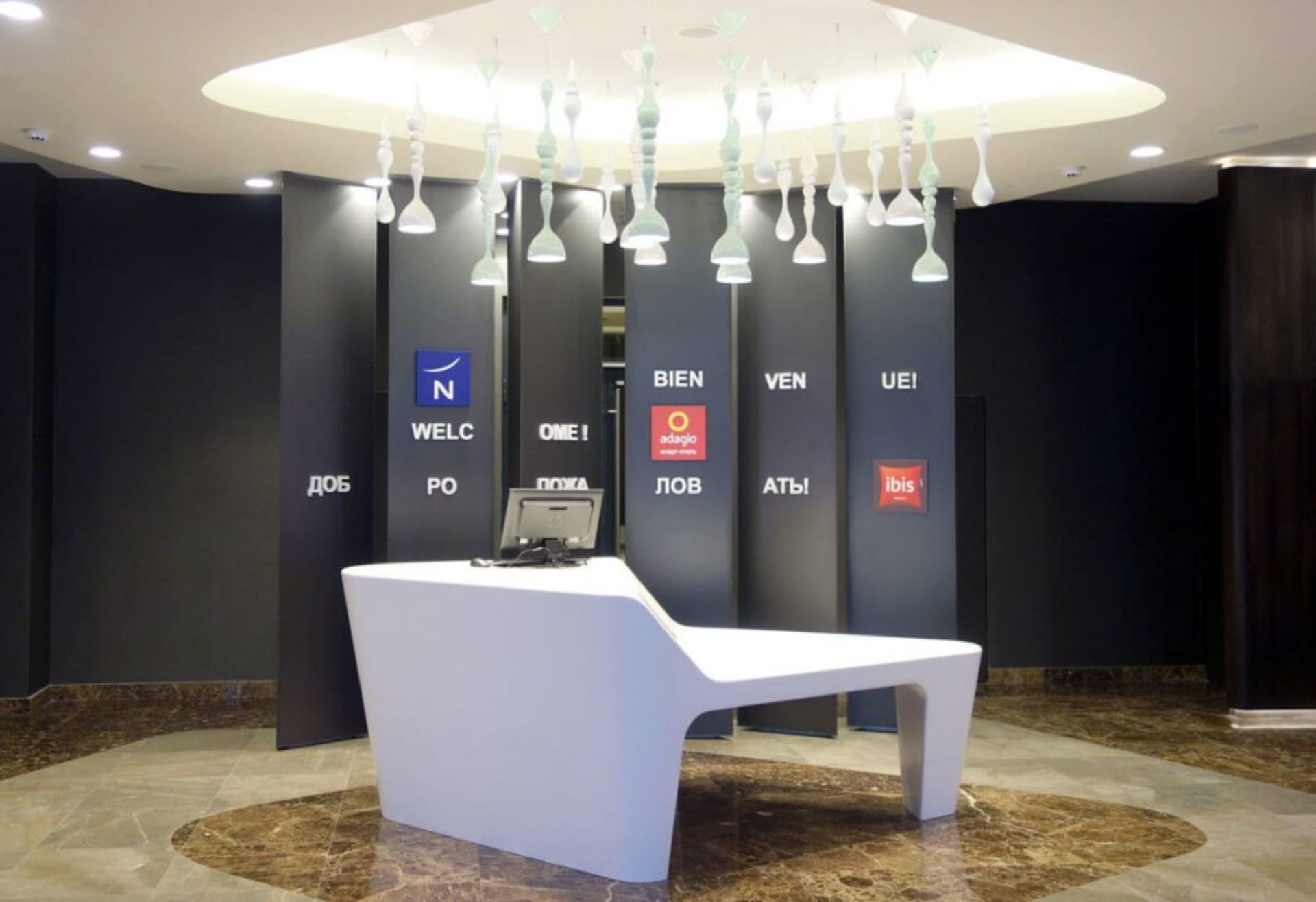A minimalist hotel reception area with a sleek white desk, black walls, and modern light fixtures.