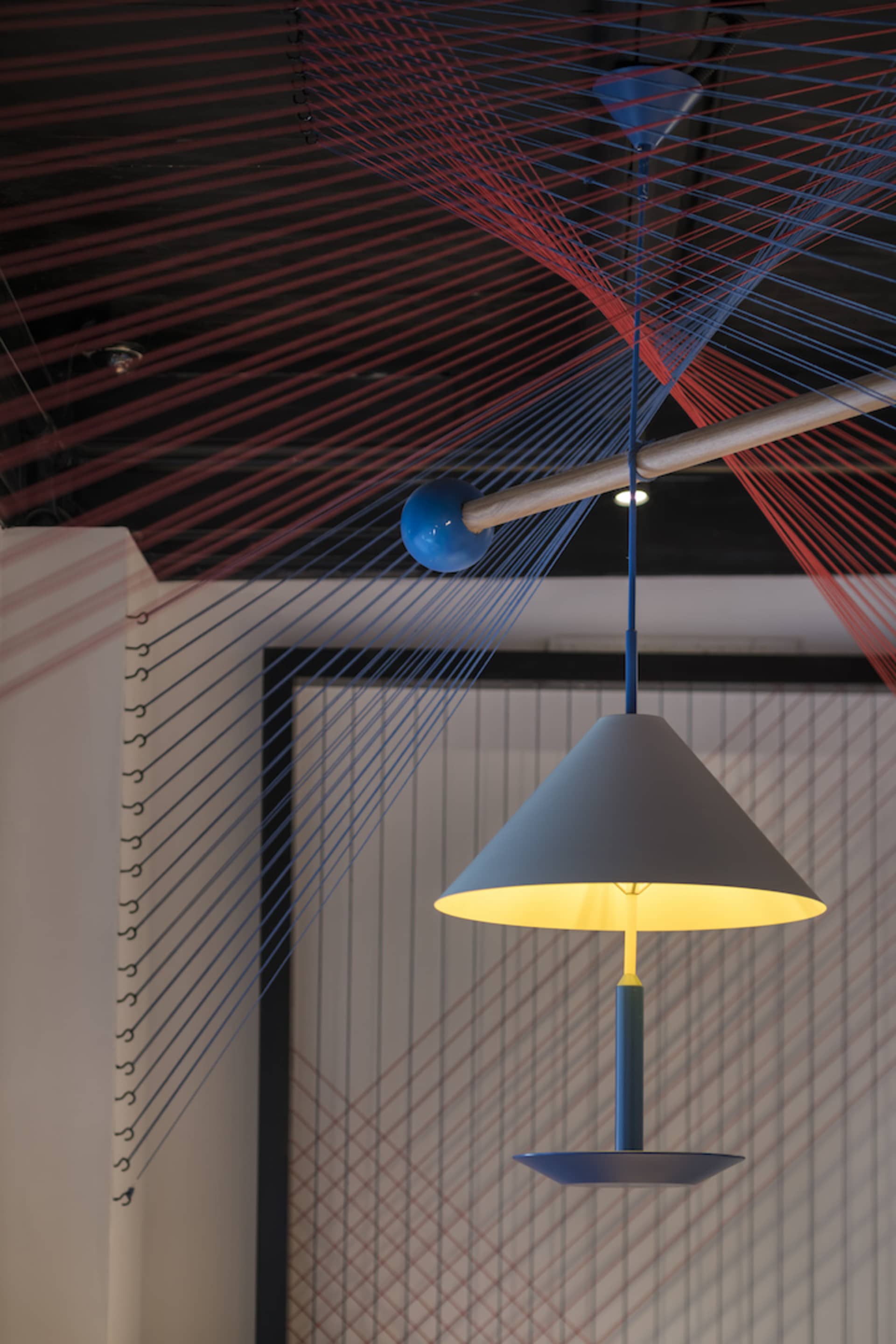 A modern light fixture hanging from the ceiling, surrounded by textile strings