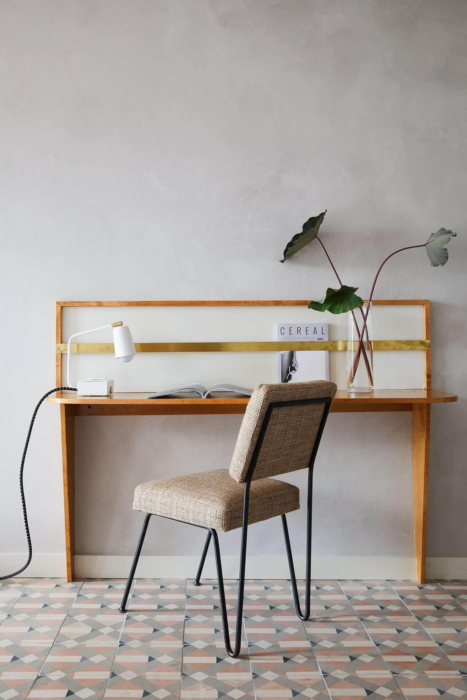 Minimalist home office workspace featuring a wooden desk with brass accents, a comfortable upholstered chair, and decorative