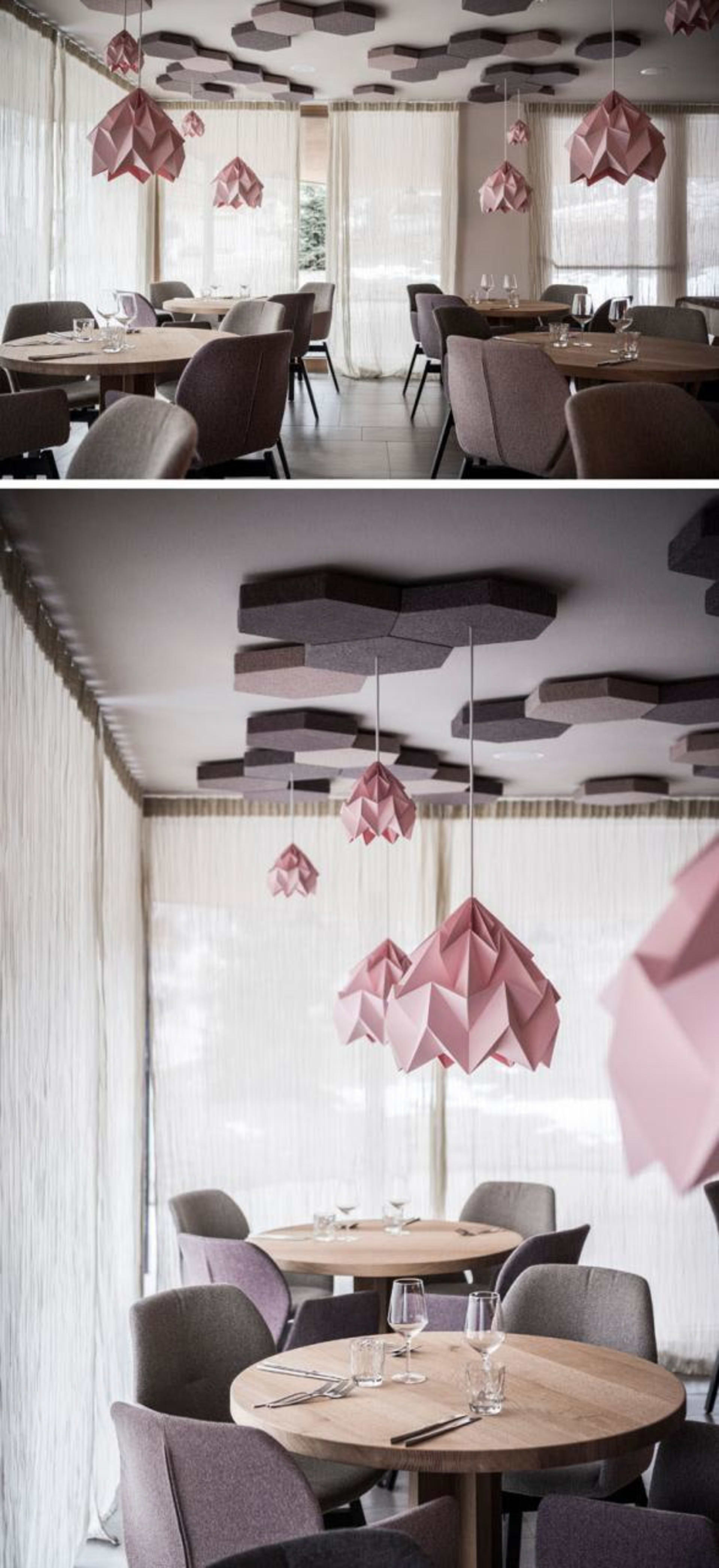 A minimalist restaurant interior featuring modern, geometric paper light fixtures hanging from the ceiling.