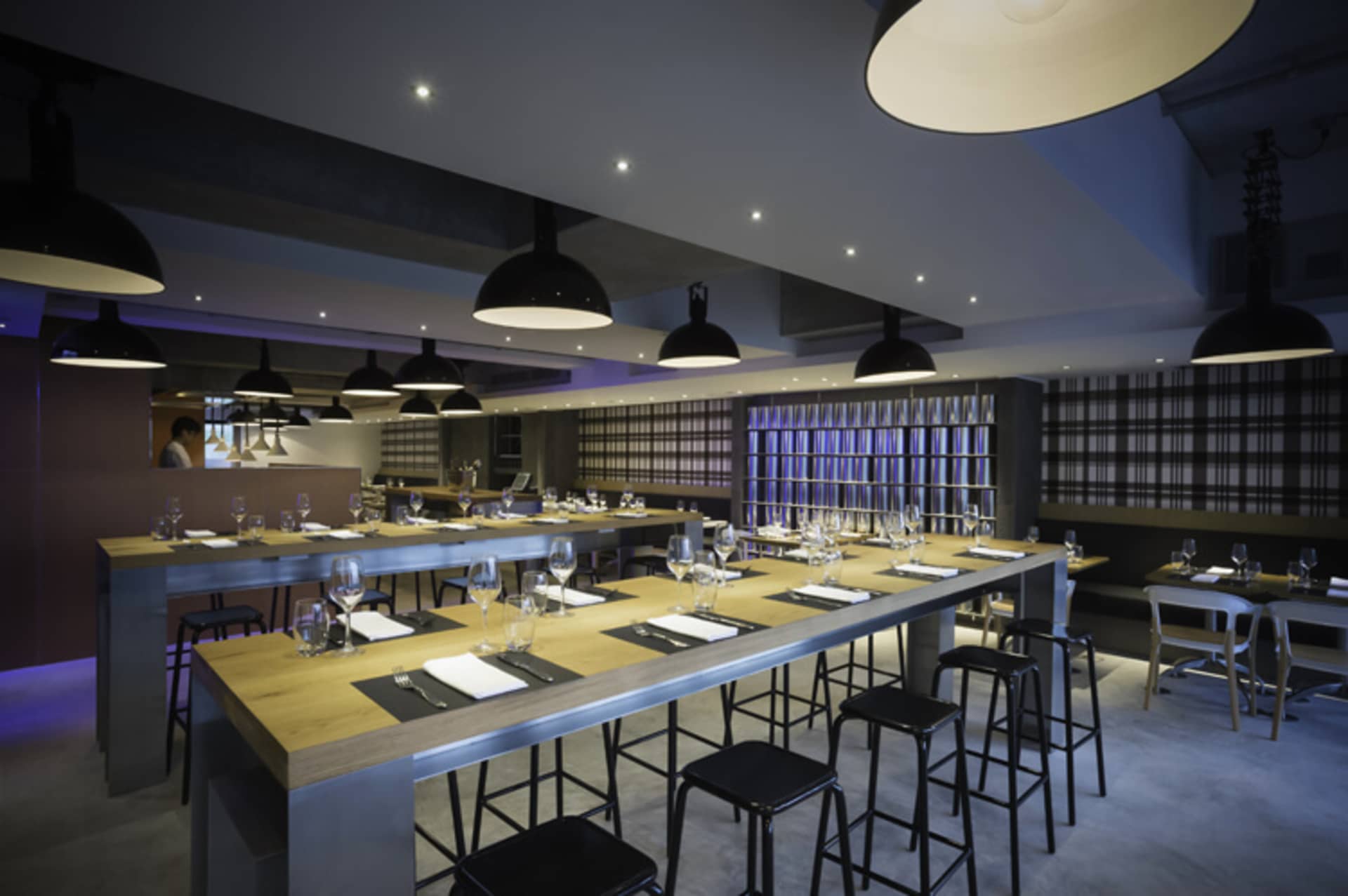 A sleek, industrial-themed restaurant interior with high tables, chairs, and pendant lights.