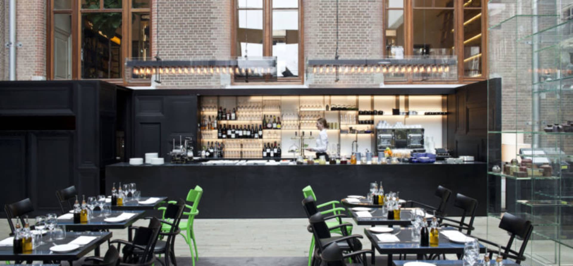 Interior design of a modern restaurant featuring a bar area with black countertops, wine bottles, and green chairs.