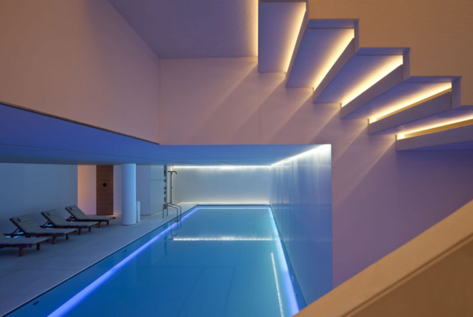 現代室內游泳池，配有玻璃牆與發光階梯。