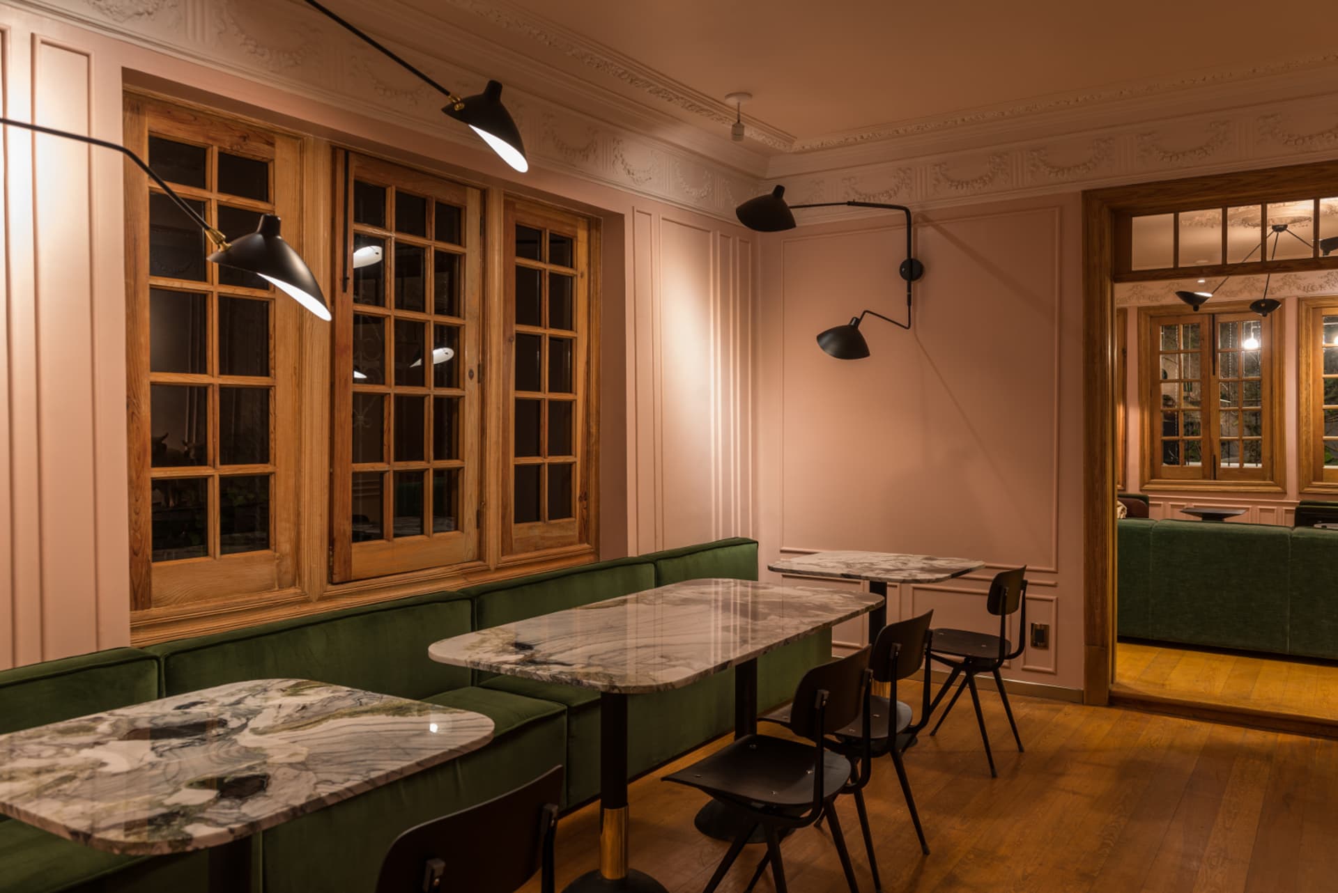 Interior of a modern cafe with marble tables, green upholstered seating, and wooden floors.