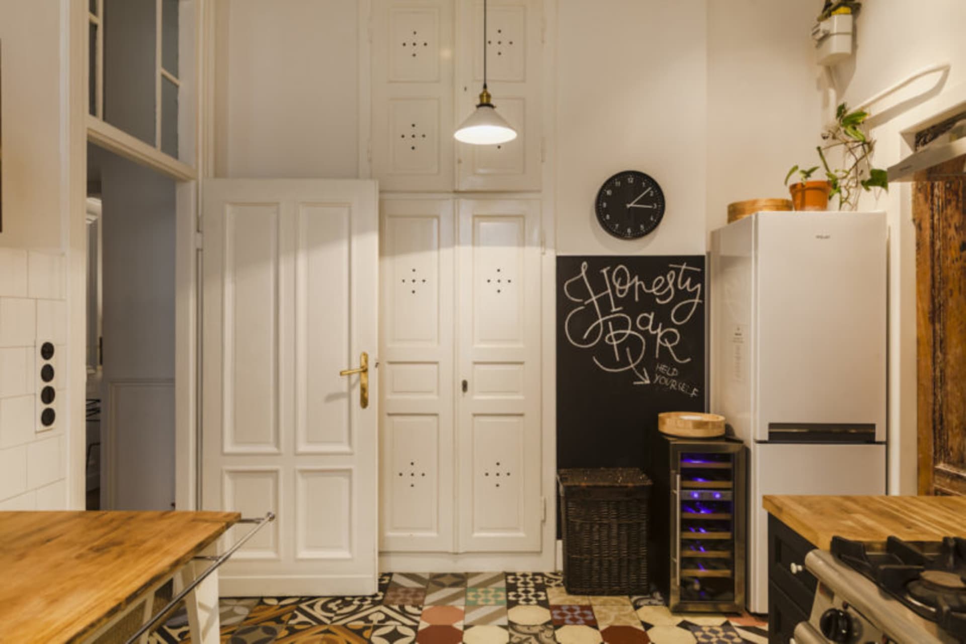 Minimalist kitchen with white furniture, patterned floor, and chalkboard with 'Honesty Bar'.