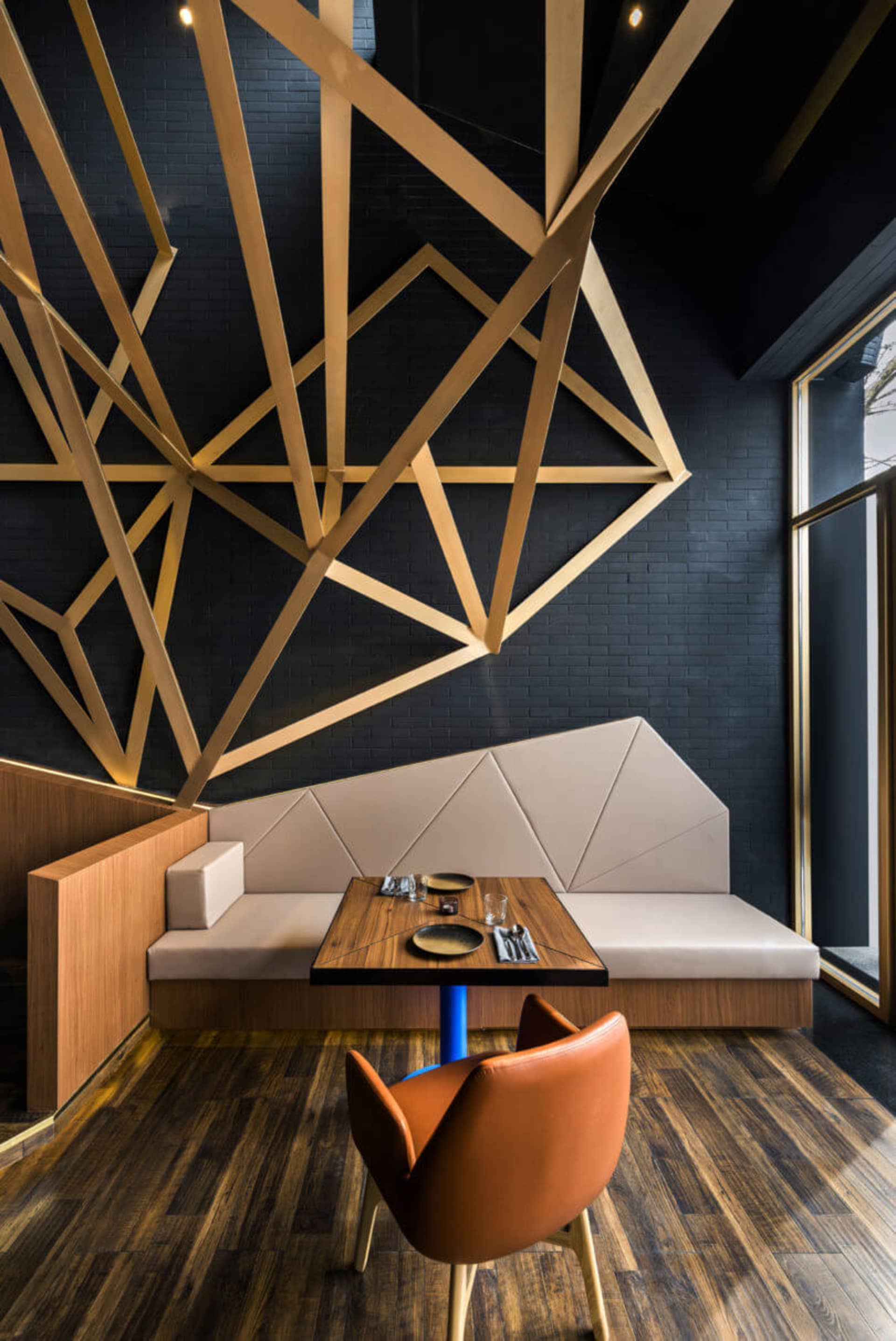 Modern industrial restaurant booth with wood and concrete materials, featuring a geometric wall design and a single orange up