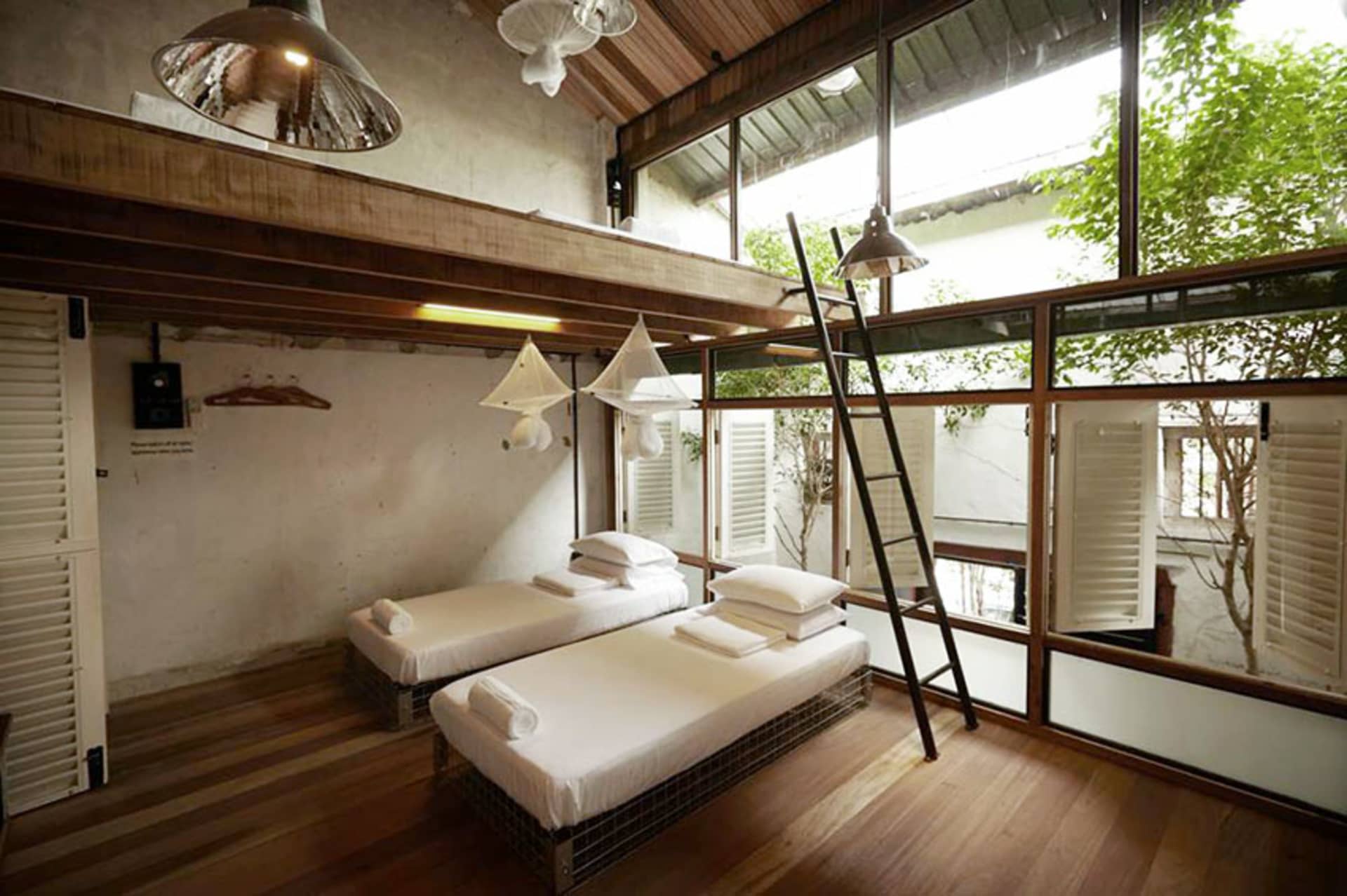 A minimalist bedroom with white bedding, wood floors, and large windows.