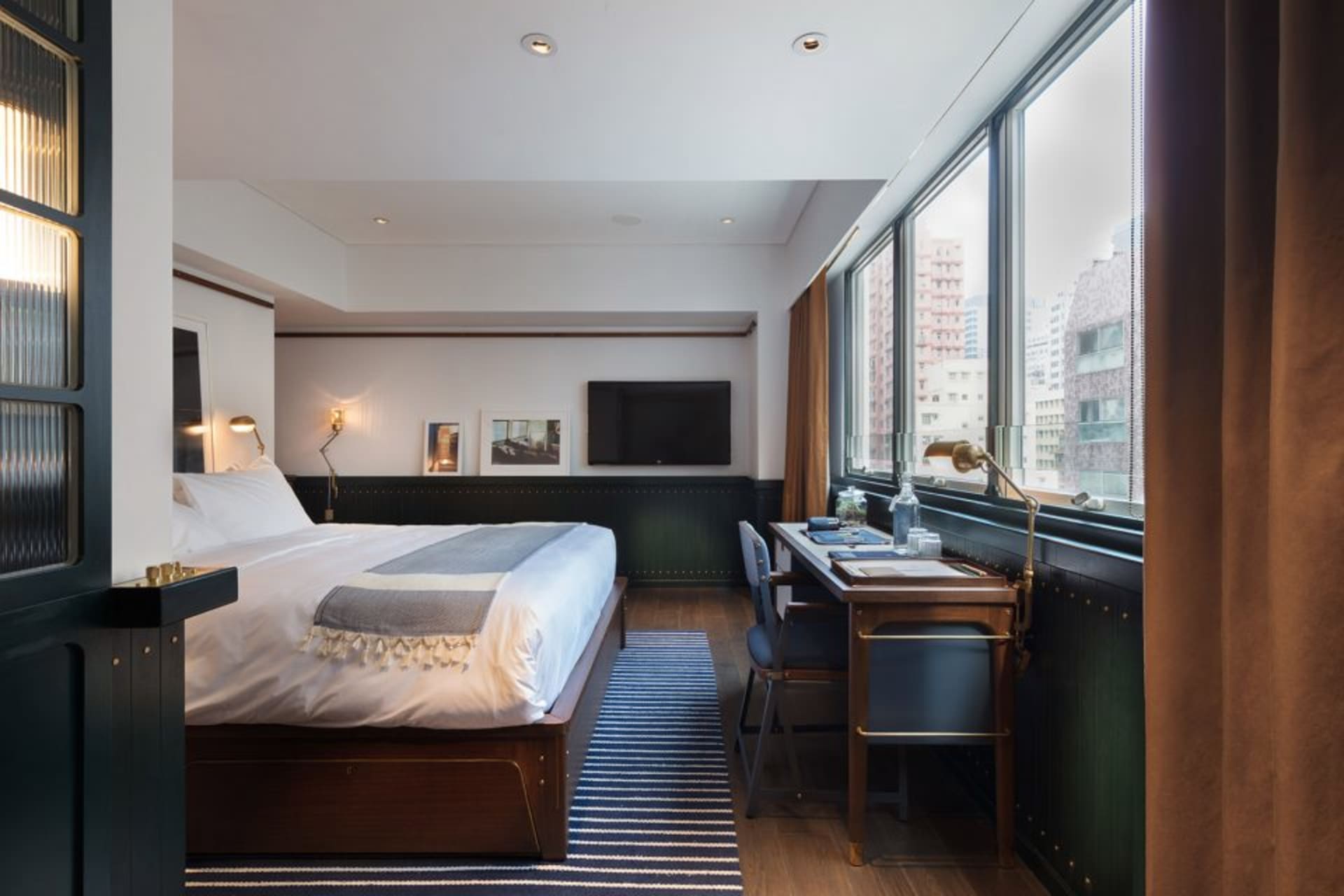 A modern minimalist bedroom with a large bed, desk, and city view.