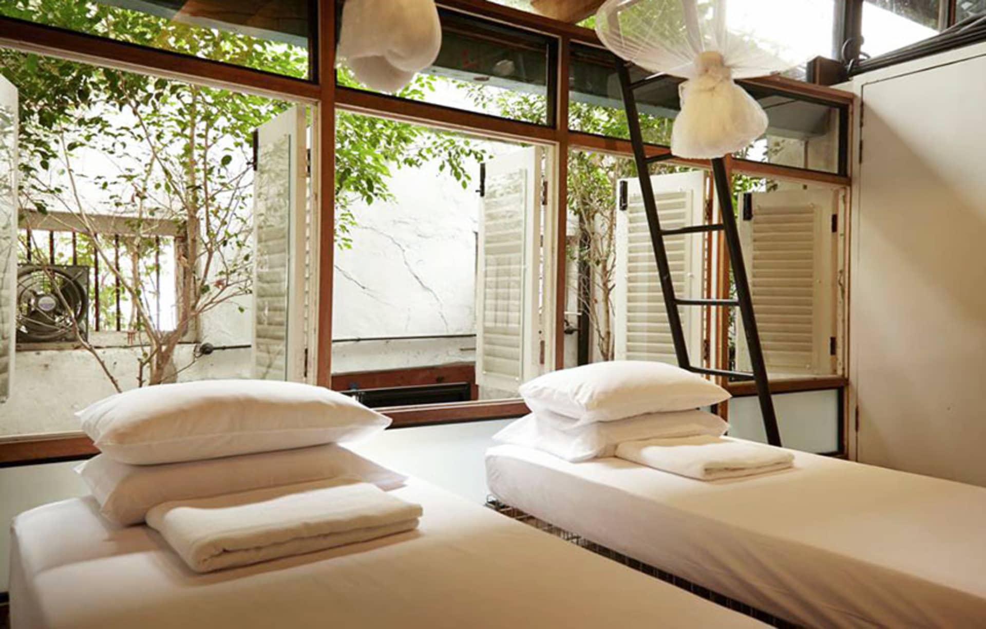 A minimalist bedroom with white bedding and organic materials, featuring twin beds with white pillows and towels, large windo