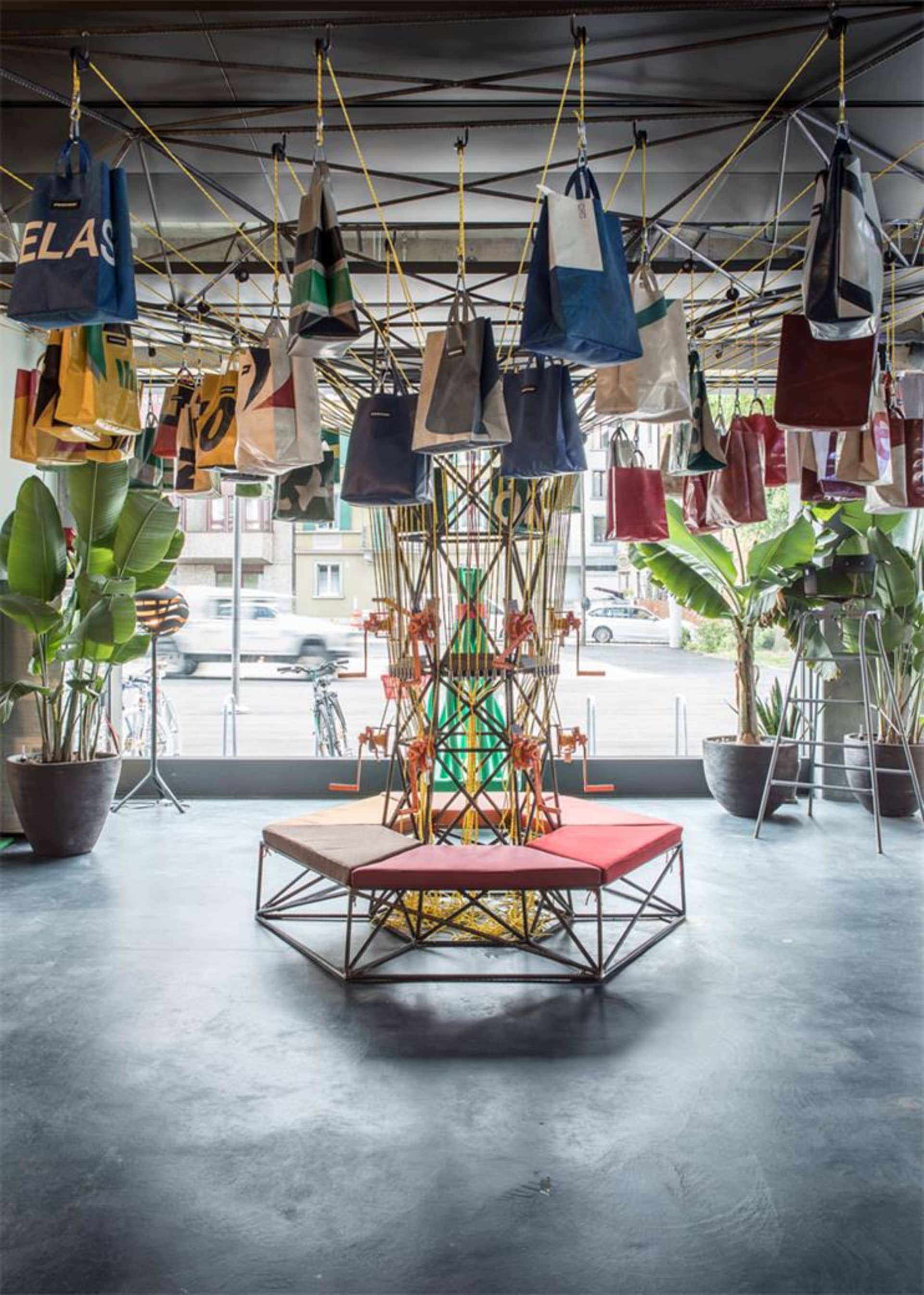 Industrial-style retail storefront with hanging fabric bags, metal structures, and glass elements.