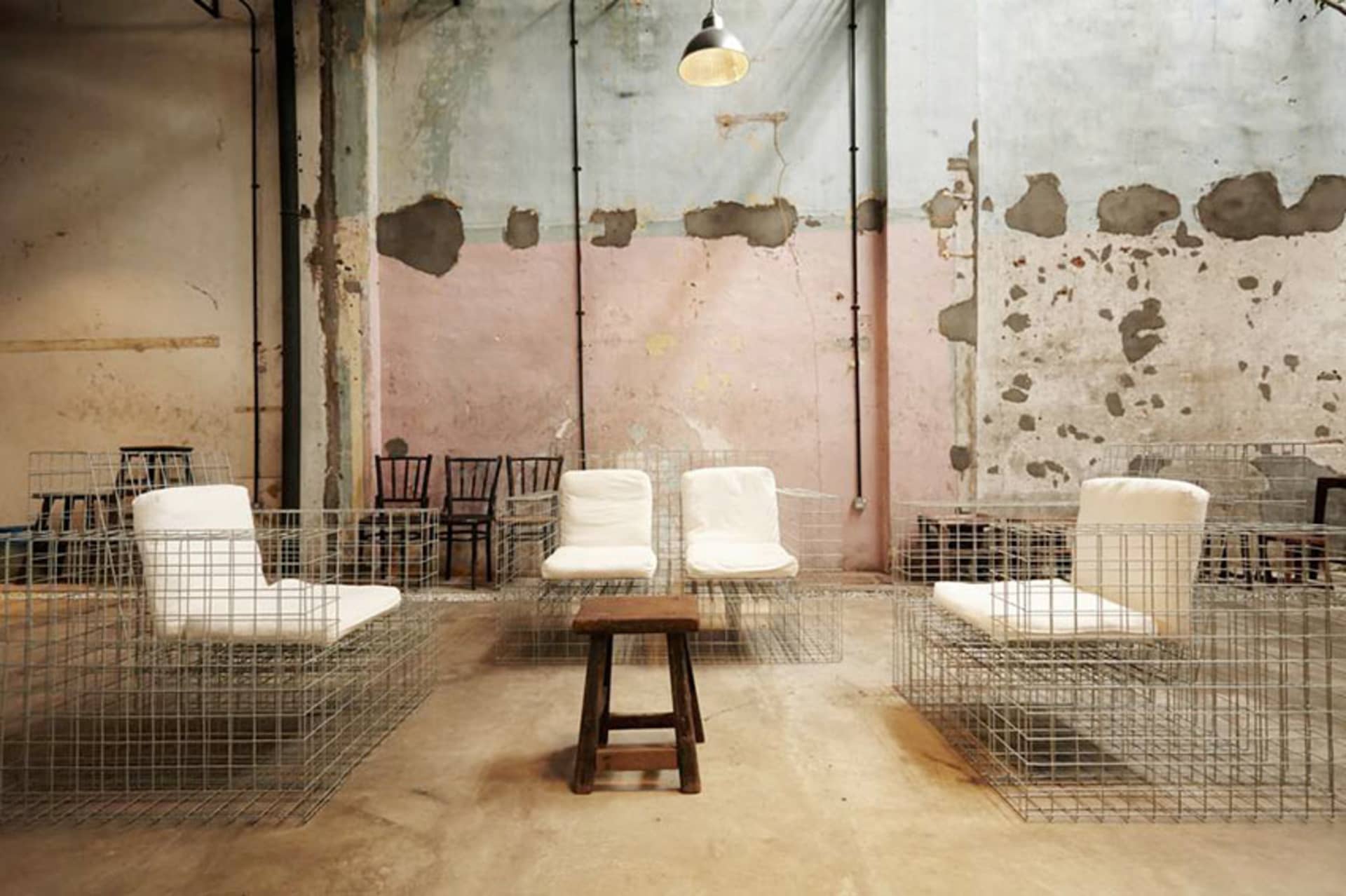 Industrial-style cafe space with metal wire cages enclosing cushioned chairs, wood stool, and exposed concrete and peeling pa