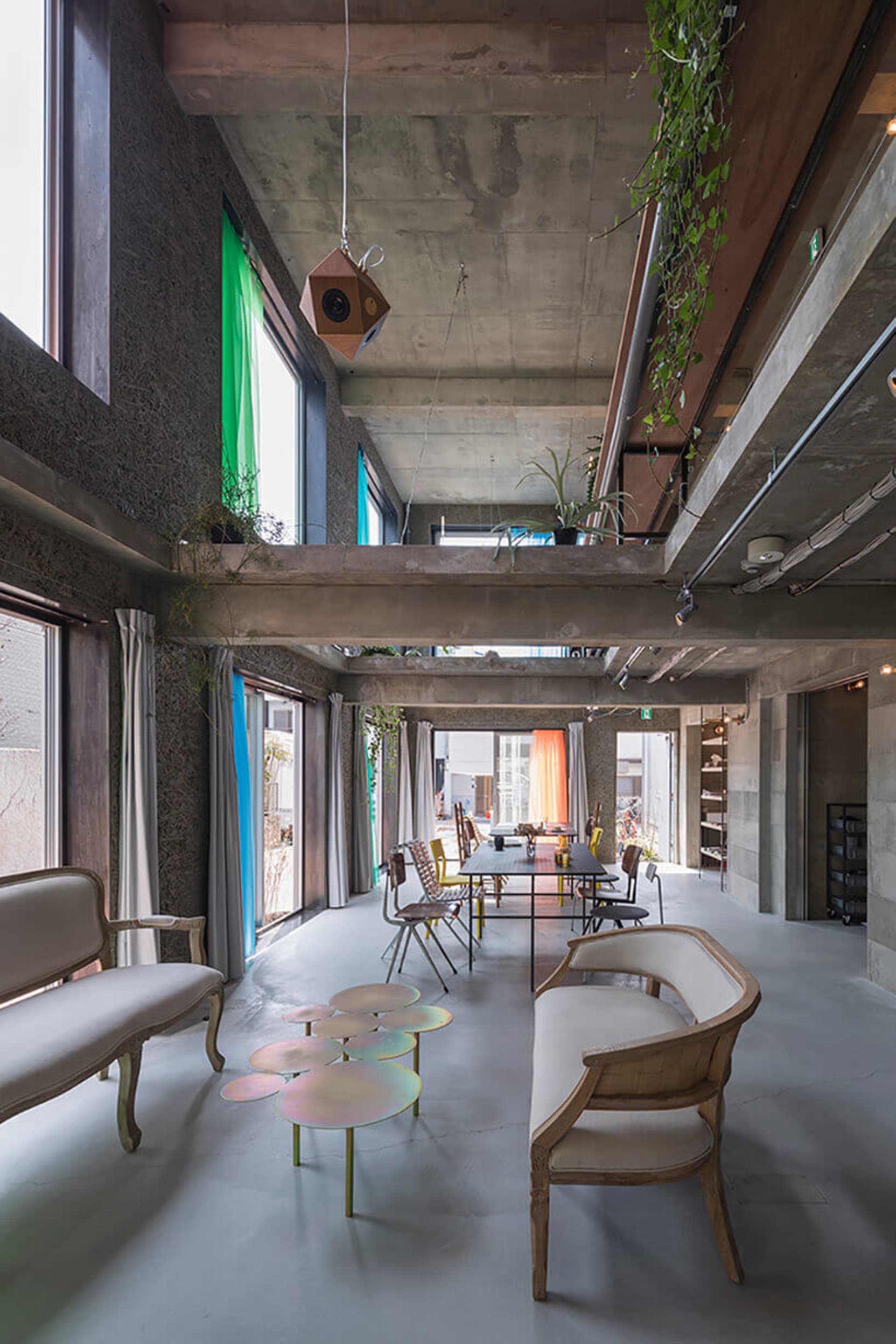 A modern, industrial-style dining room with concrete walls and ceiling, featuring a long table and distinctive coffee tables
