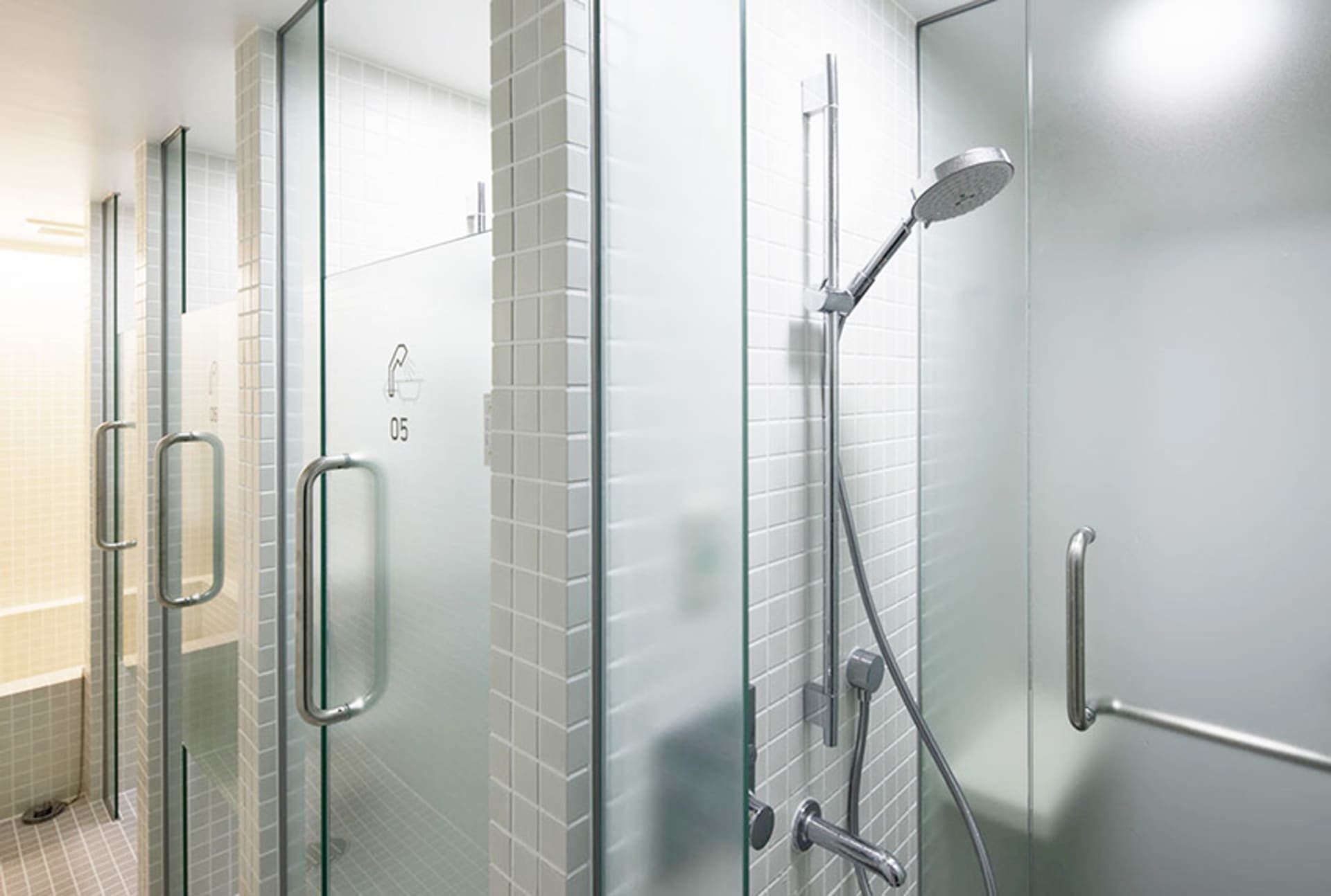 A modern bathroom with glass shower enclosures, metal hardware, and white tiled walls.