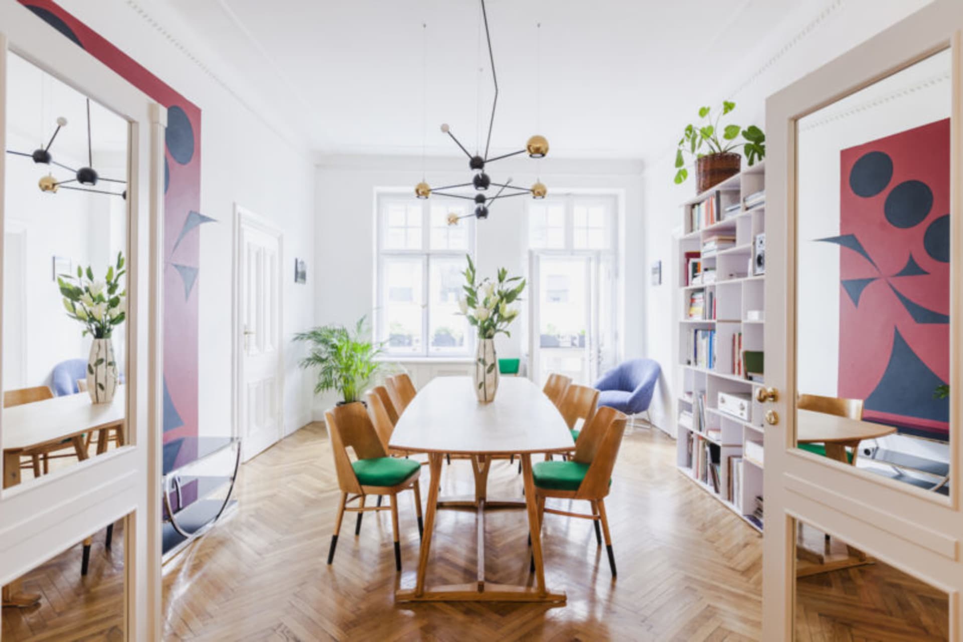 A modern living room with hardwood floors, wooden furniture, glass chandelier, and greenery.