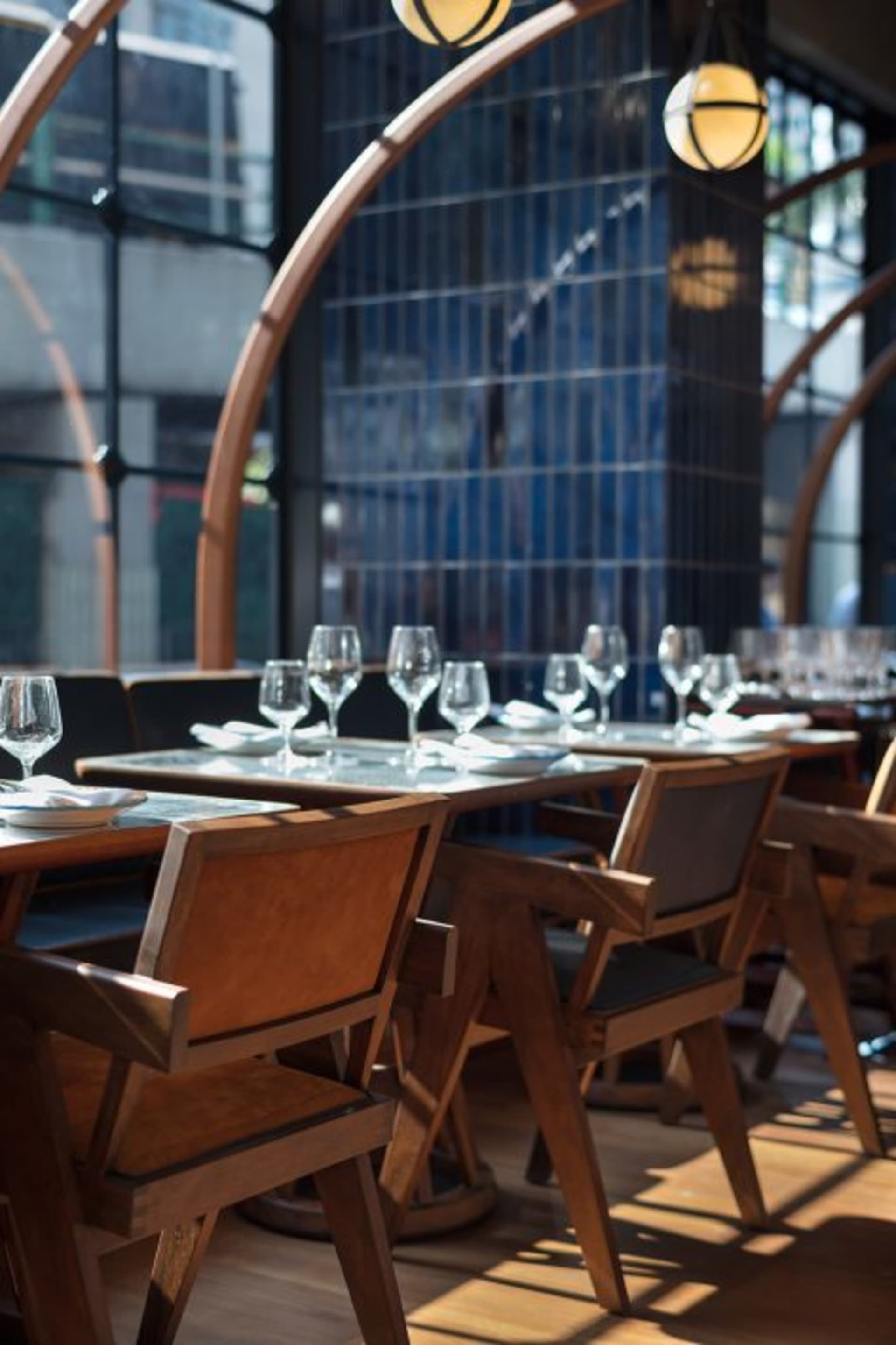 A modern restaurant interior with wooden chairs and tables, glassware, and minimalist decor.