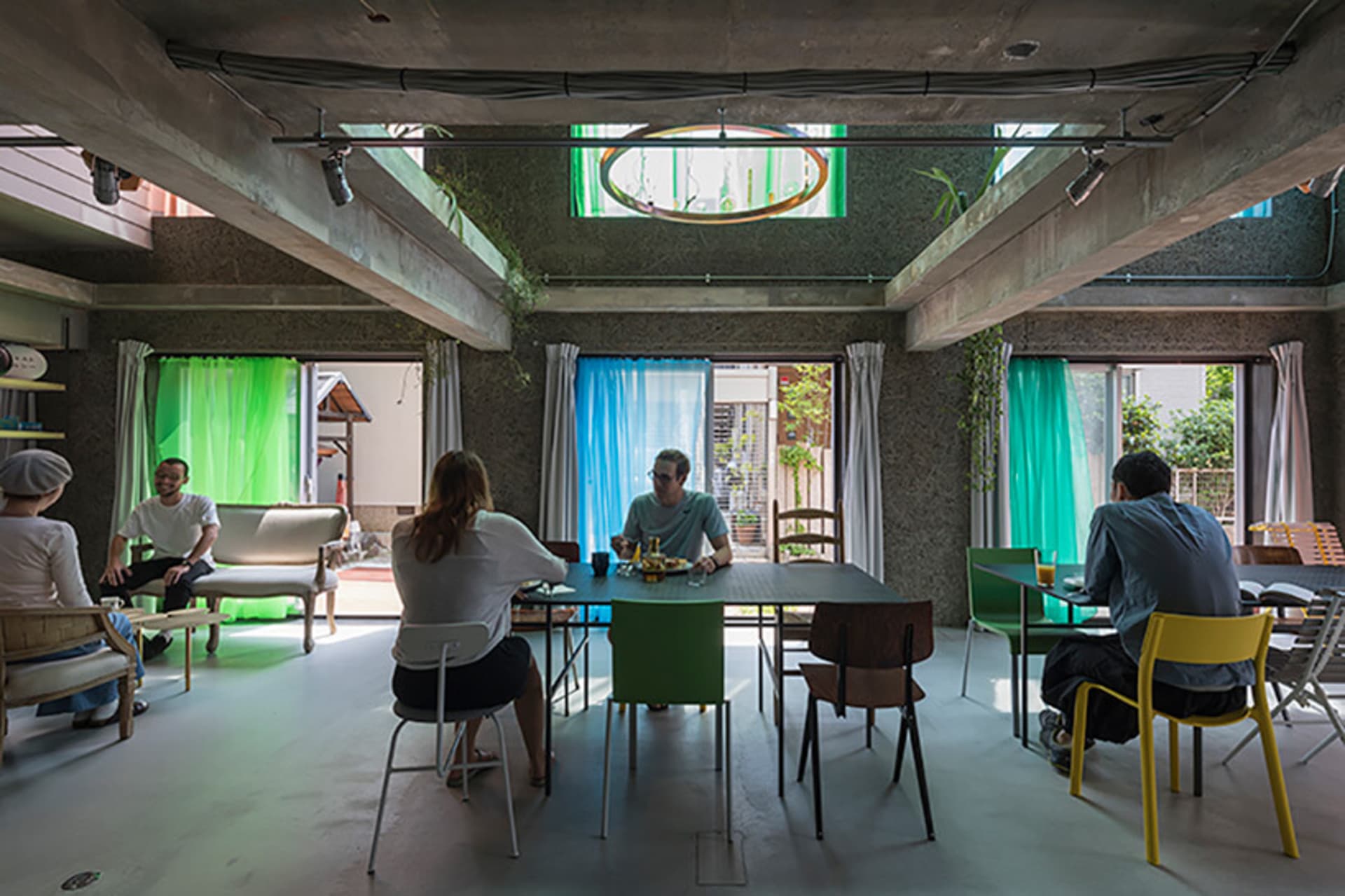 Interior view of a cafe with concrete walls, glass windows, fabric curtains, and green plants.