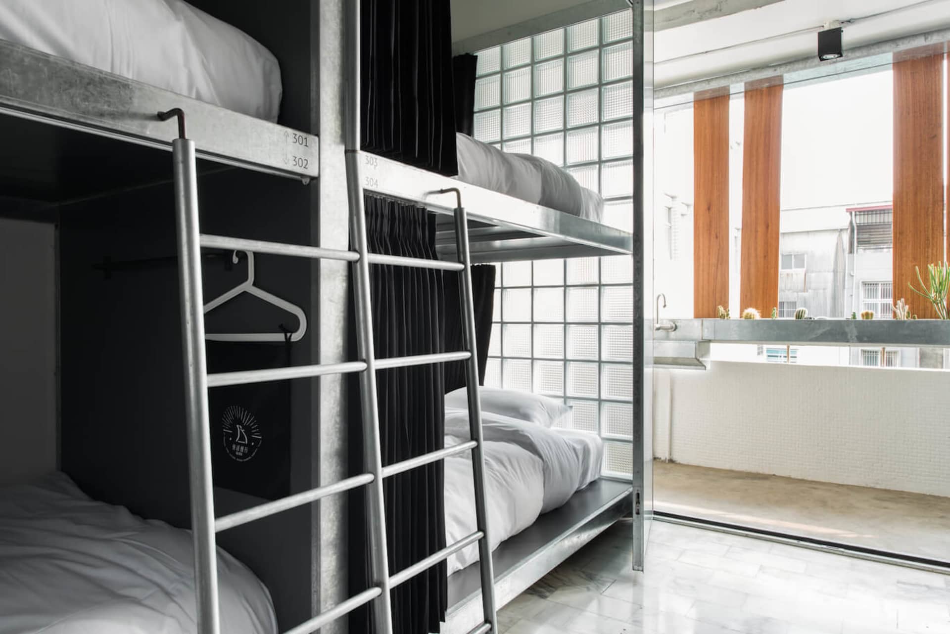 Metallic bunk beds with white bedding in an industrial-style hostel bedroom