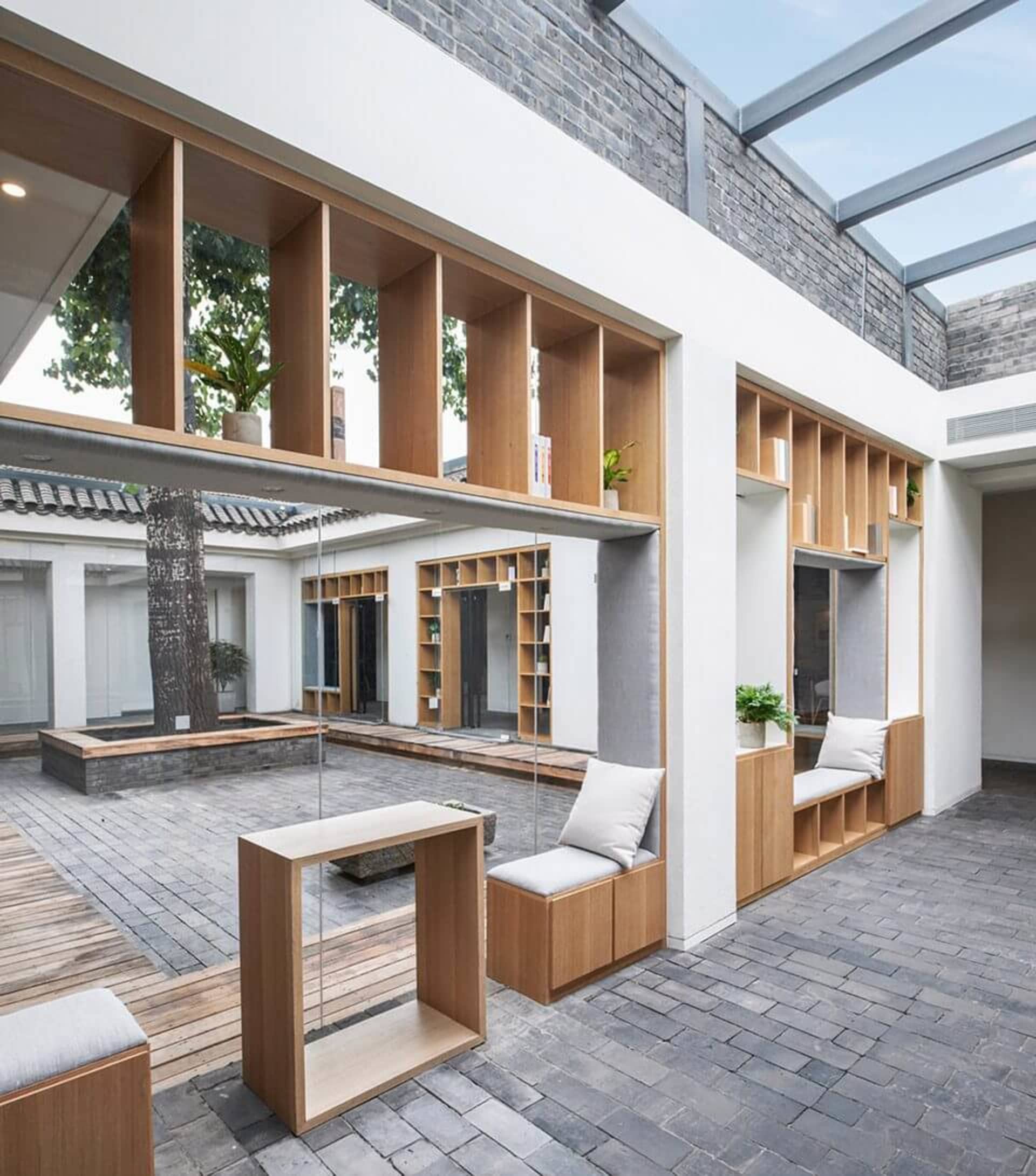 A minimalist courtyard library featuring wooden shelves, concrete pavers, and plants.