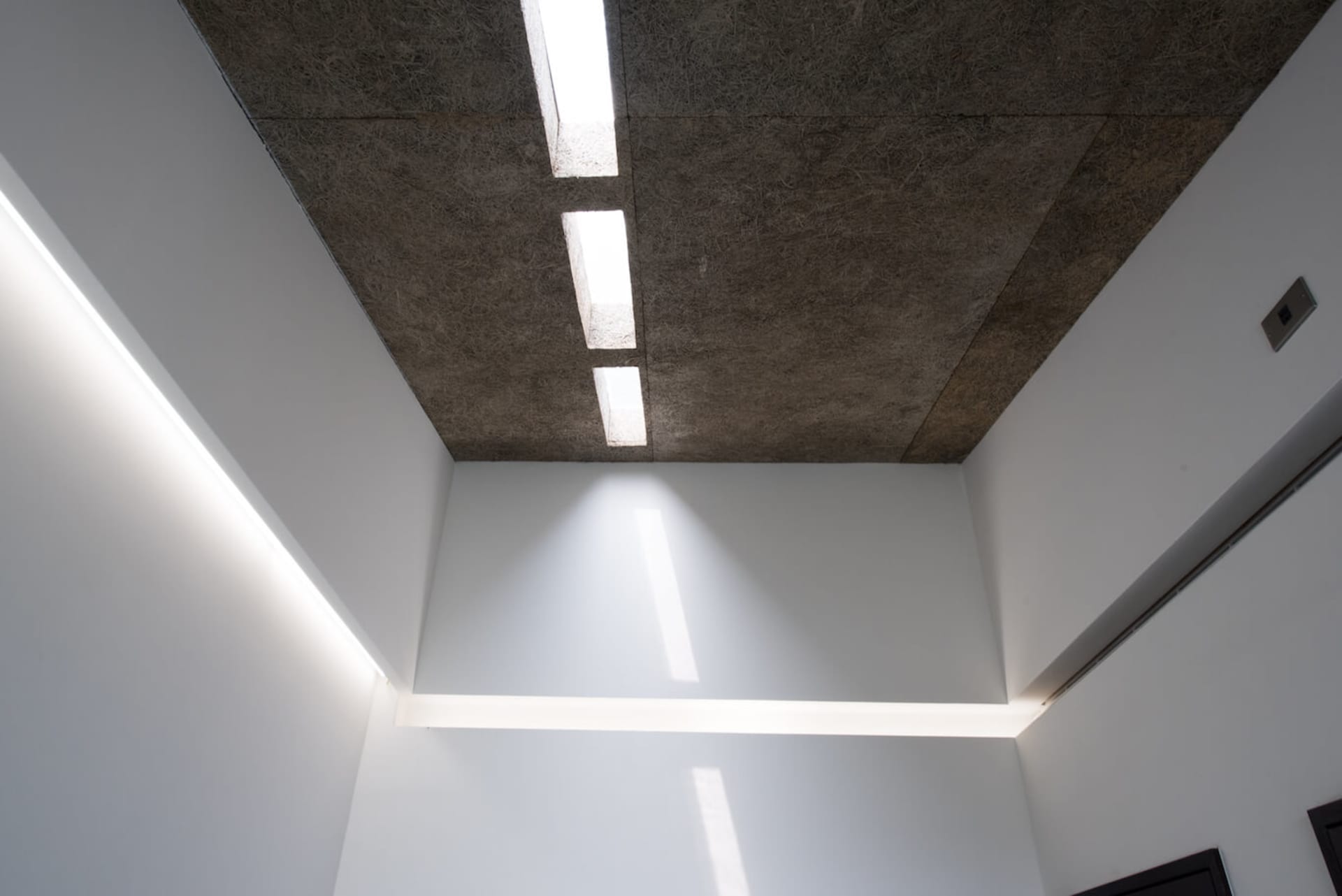 Modern interior design featuring textured concrete ceiling panels and linear lighting fixtures.
