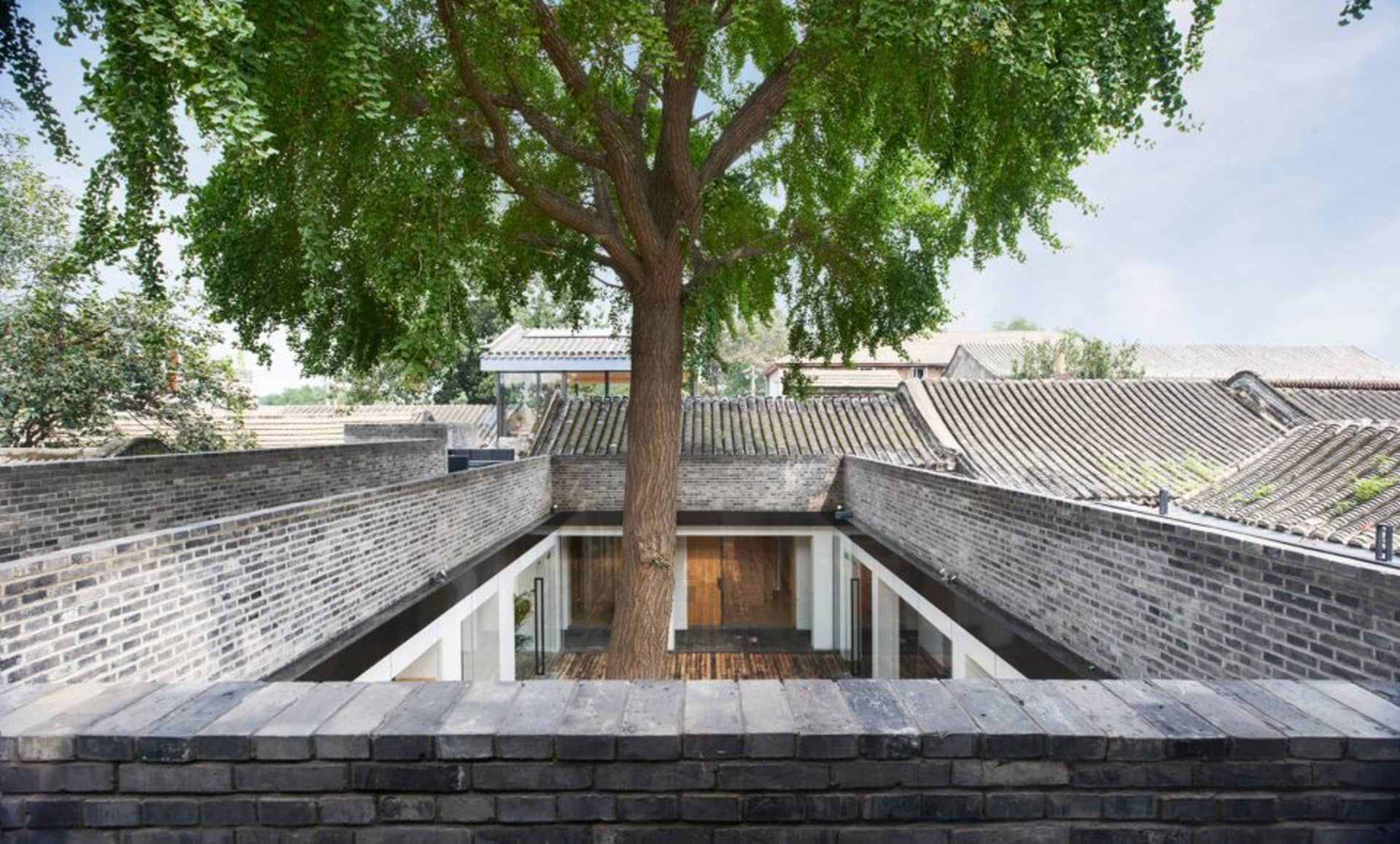 Traditional Chinese architecture featuring brick walls and a central tree.