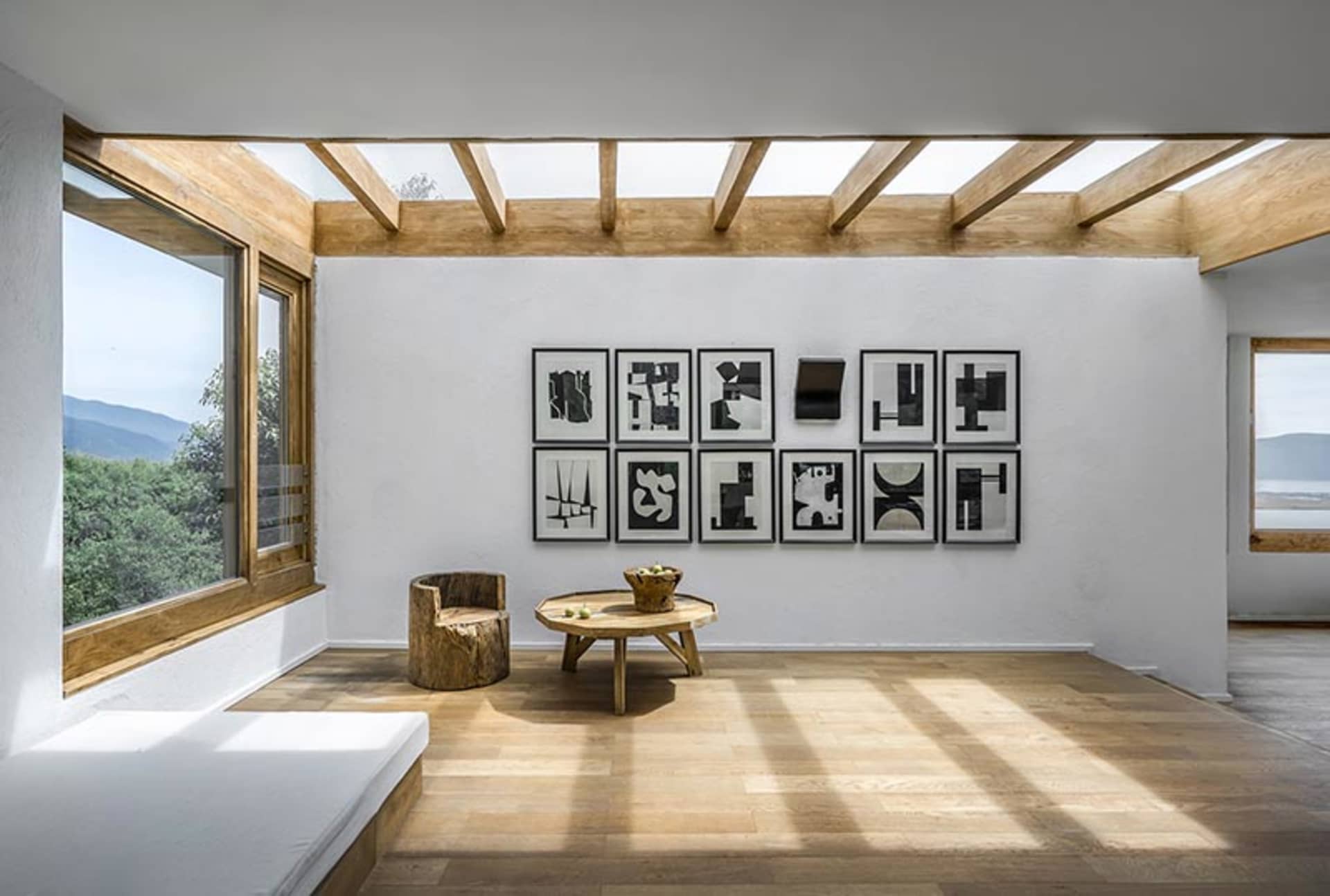 Modern, minimalist living room featuring abstract black-and-white art on a white wall, wooden floors, a rustic stump chair, a