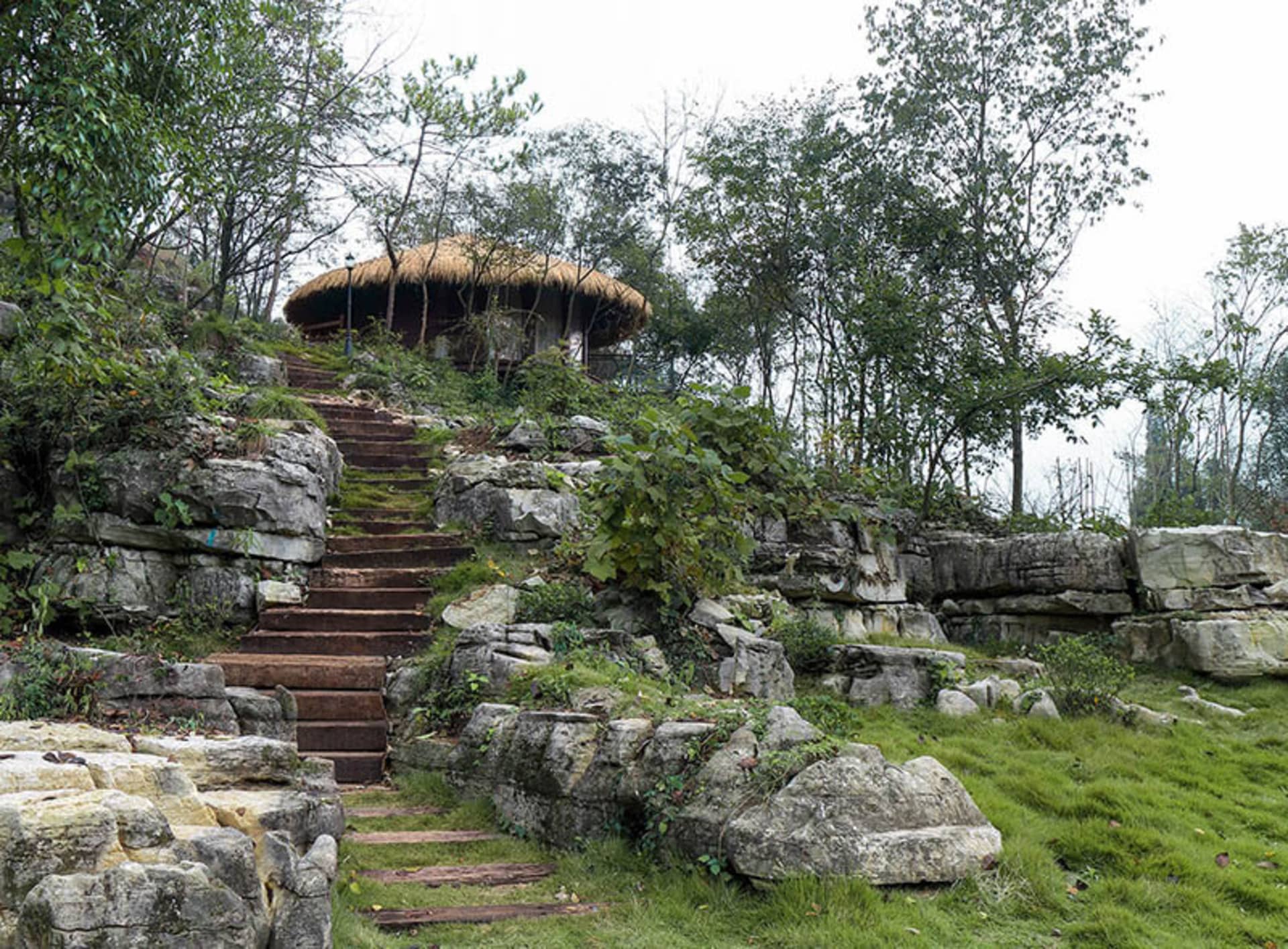 一座鄉村風小屋坐落於石階之上,四周環繞綠意盎然的自然景觀。