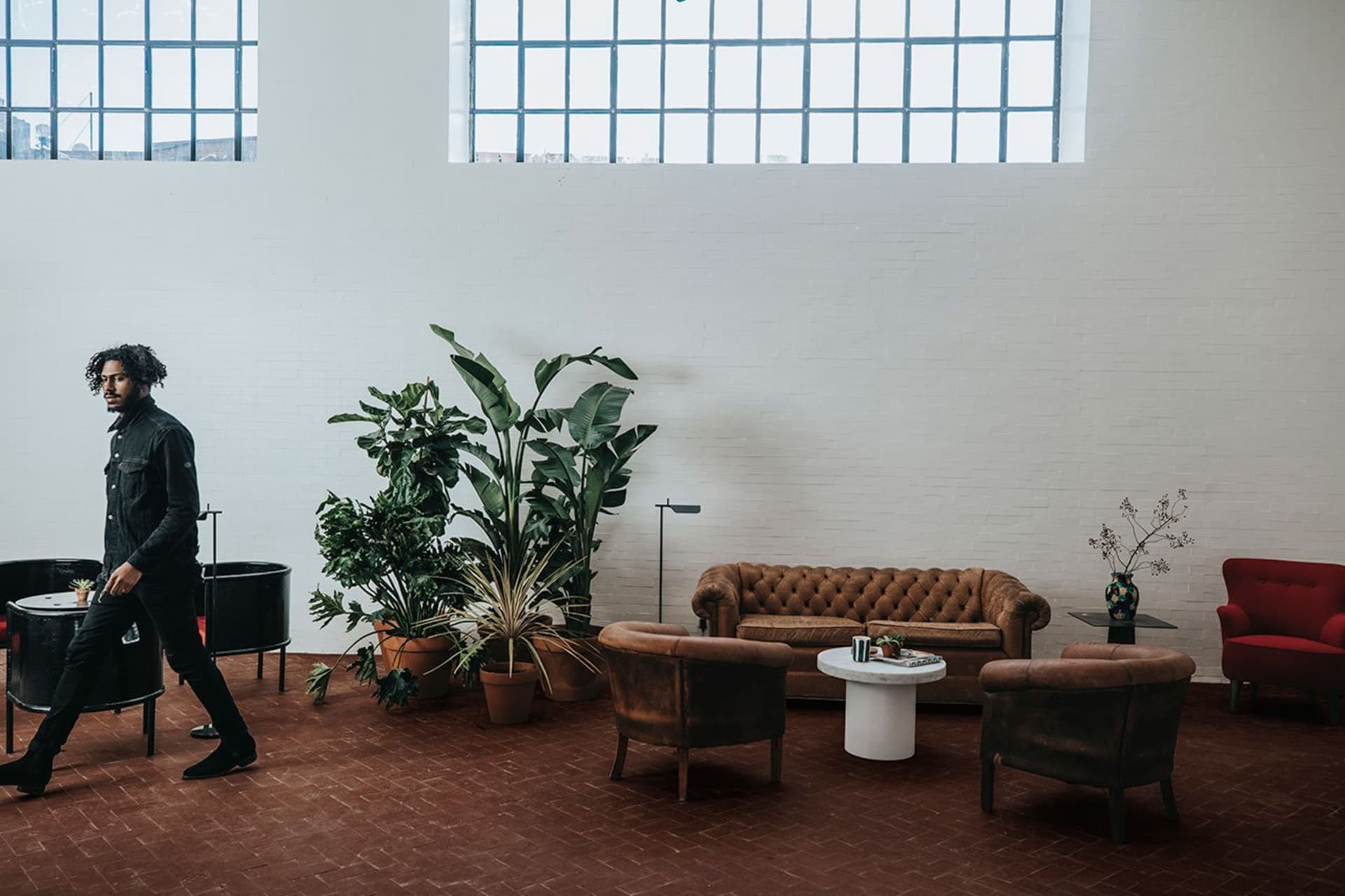 A spacious, industrial-style lobby with a brown brick floor, various indoor plants, and leather furniture.