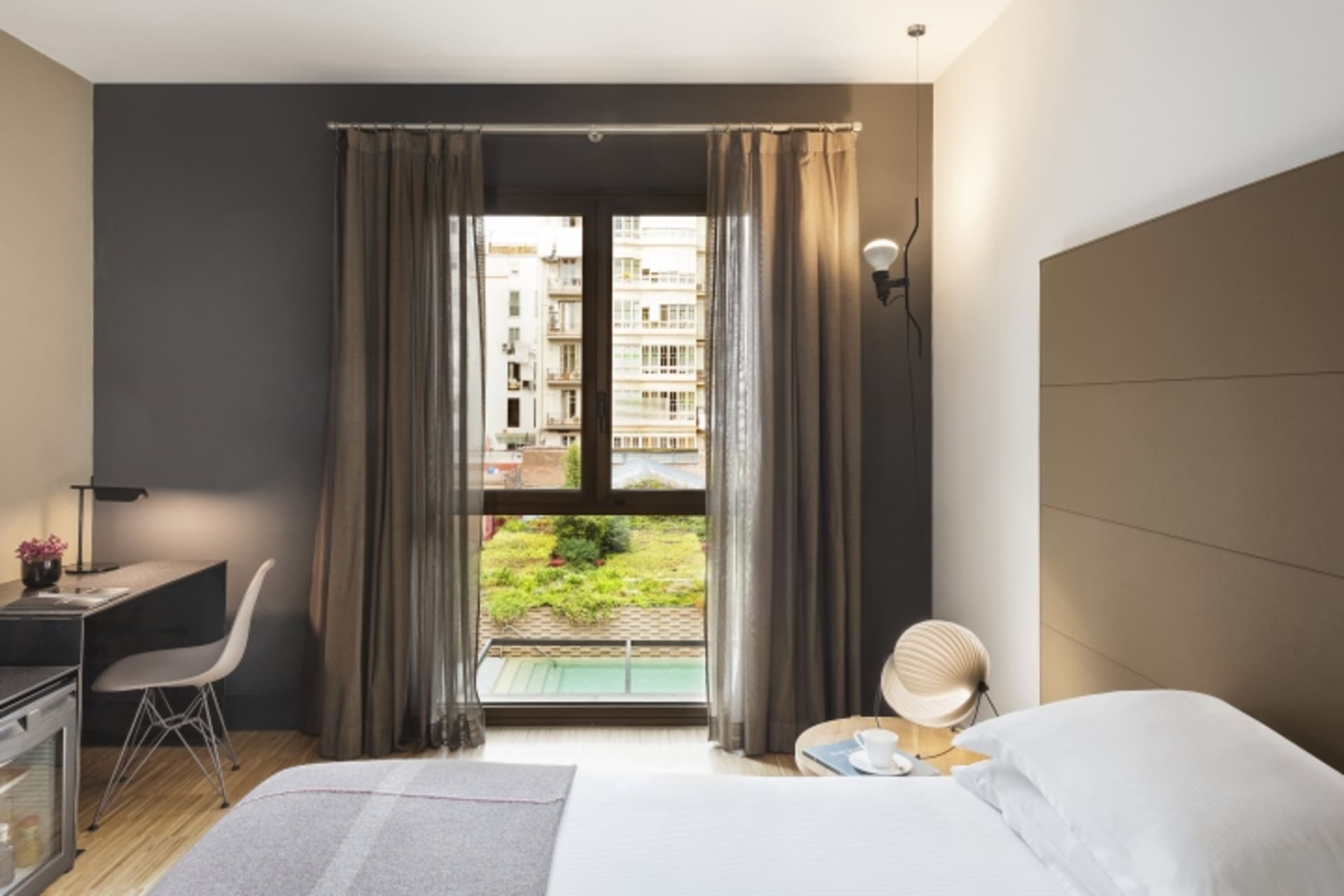 A modern hotel room with textured cotton blend materials, featuring a king-sized bed, desk, and large window overlooking a ga