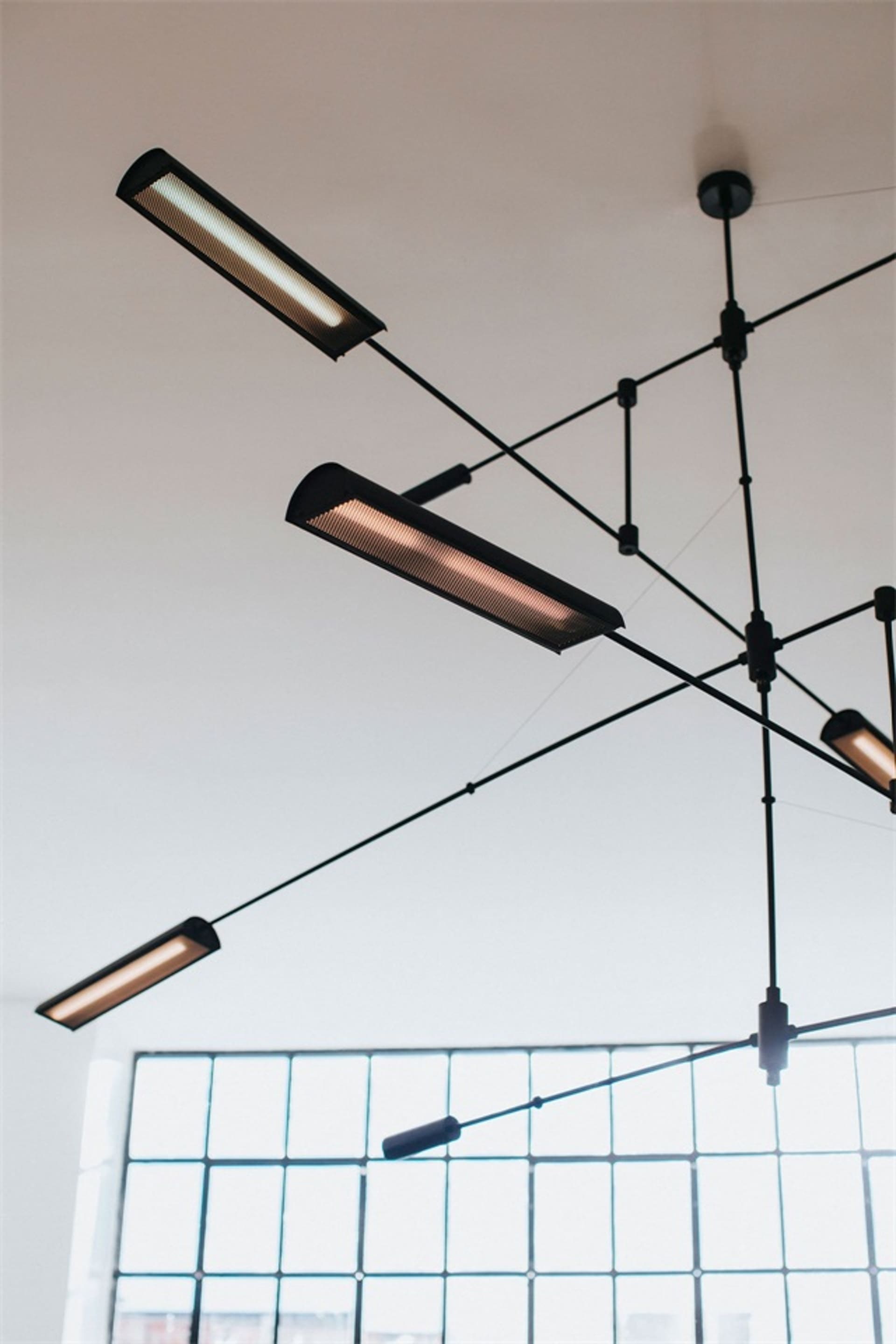 Modern industrial-style office ceiling lights hanging from metal wire framing system.