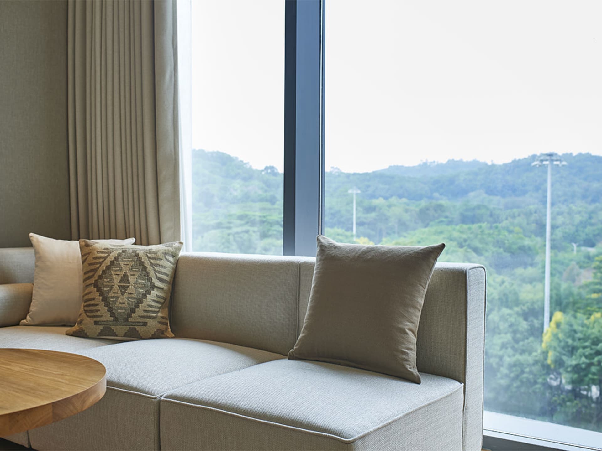 Modern living room with fabric cushions and a large window overlooking green hills.