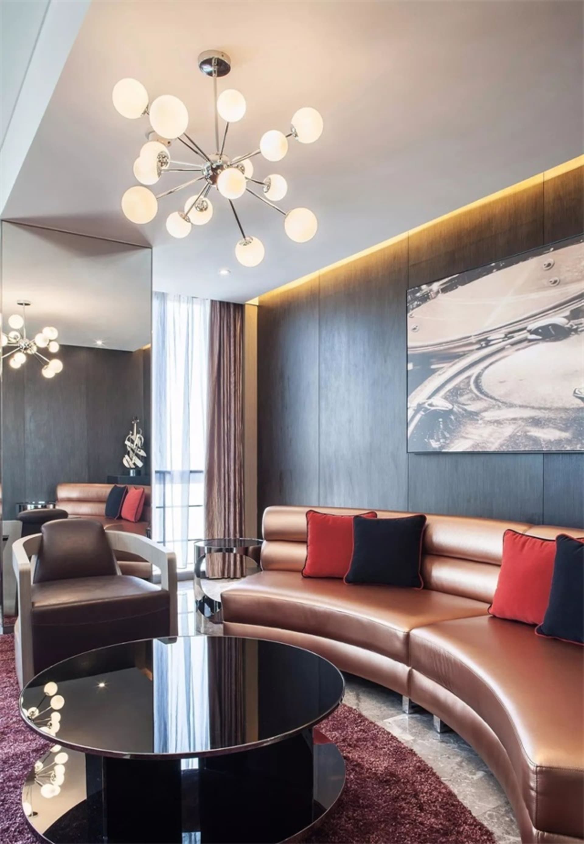 Modern living room featuring a curved leather sofa with red and black throw pillows, a black round coffee table, and a chande