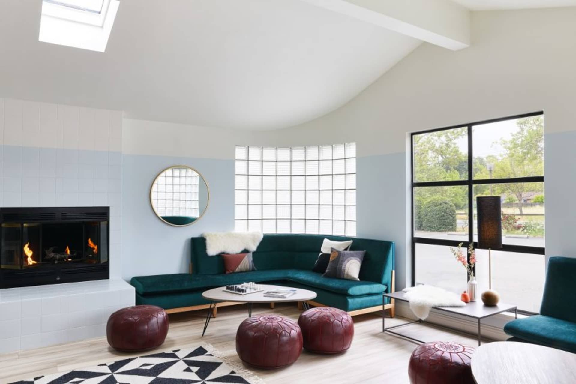 A modern living room featuring a blue velvet couch, round coffee table, and concrete floor with geometric rug, illuminated by