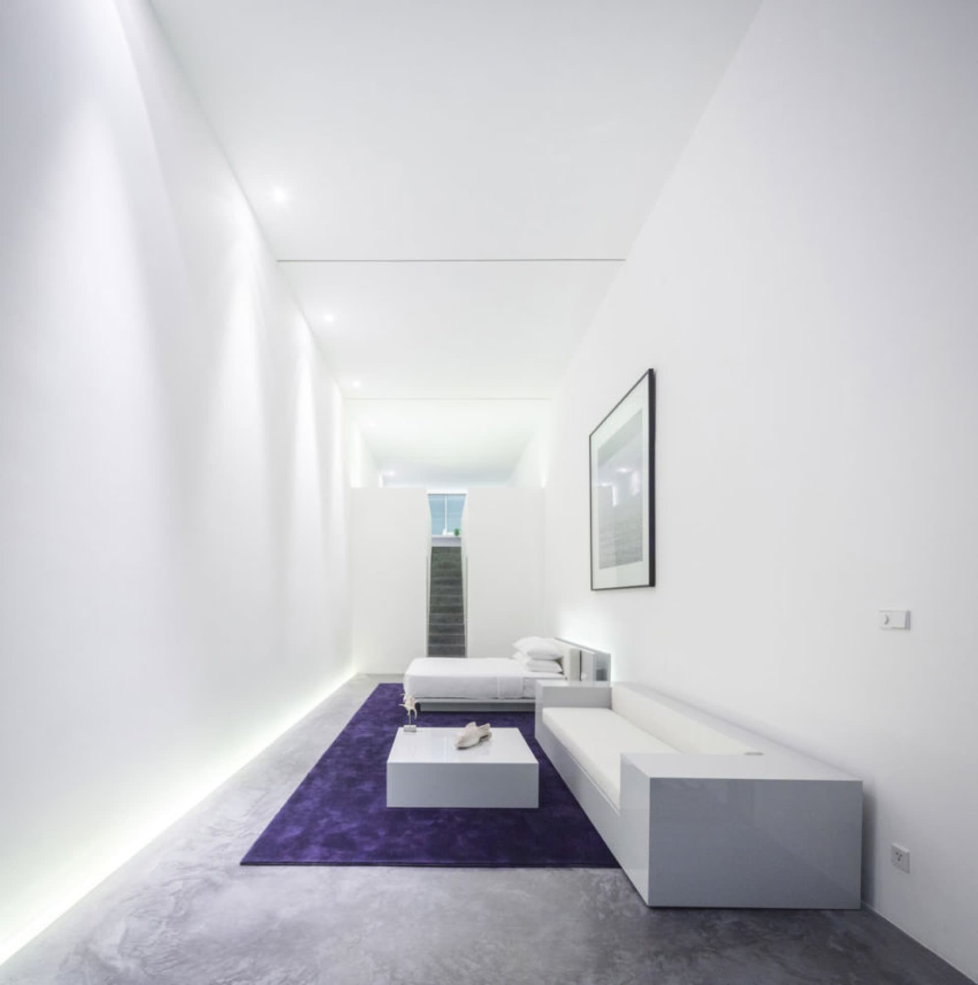 A minimalistic bedroom with concrete flooring and white furniture