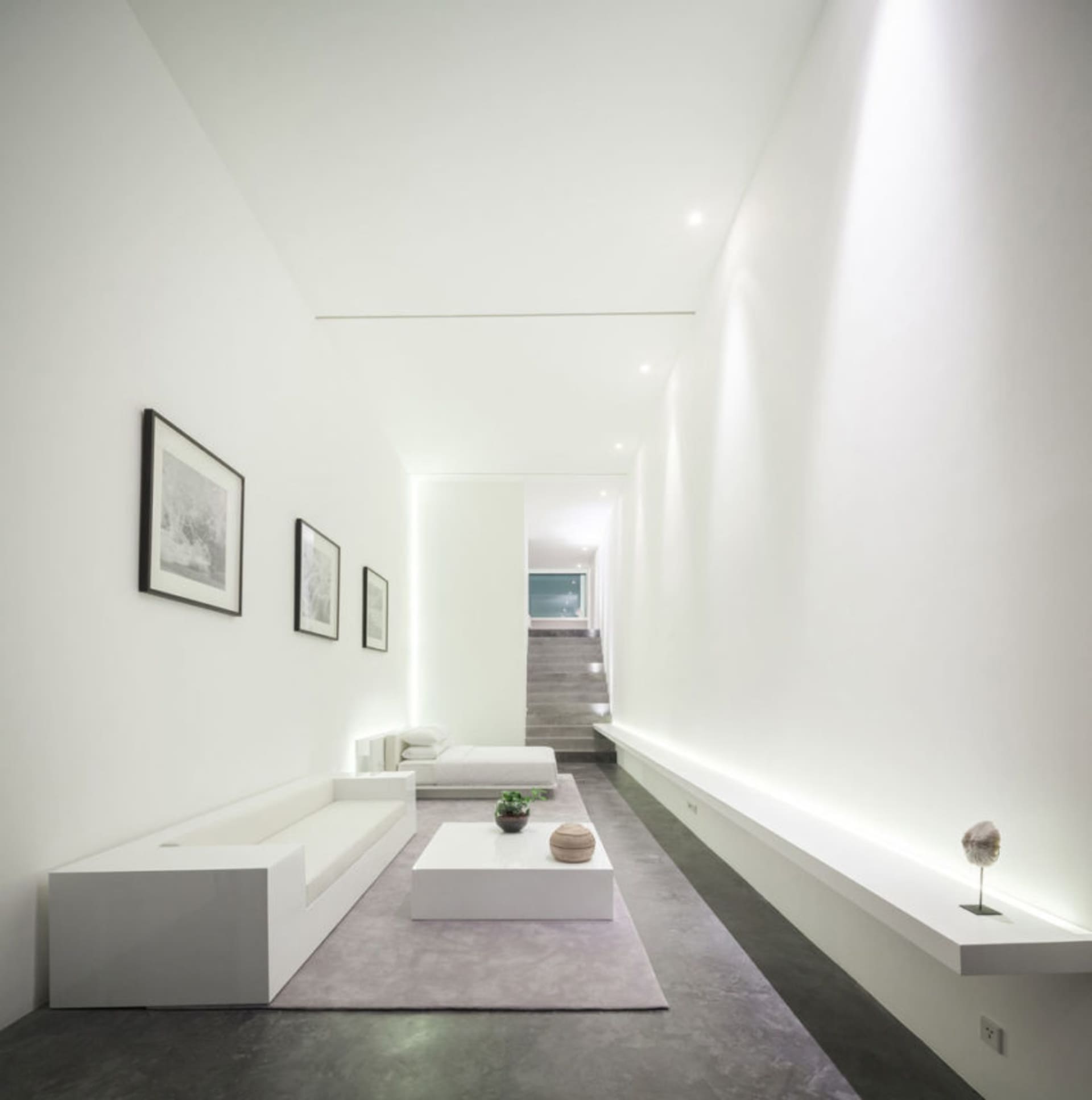 A modern minimalist living room featuring a concrete floor and walls, with white furniture and minimalist decor.