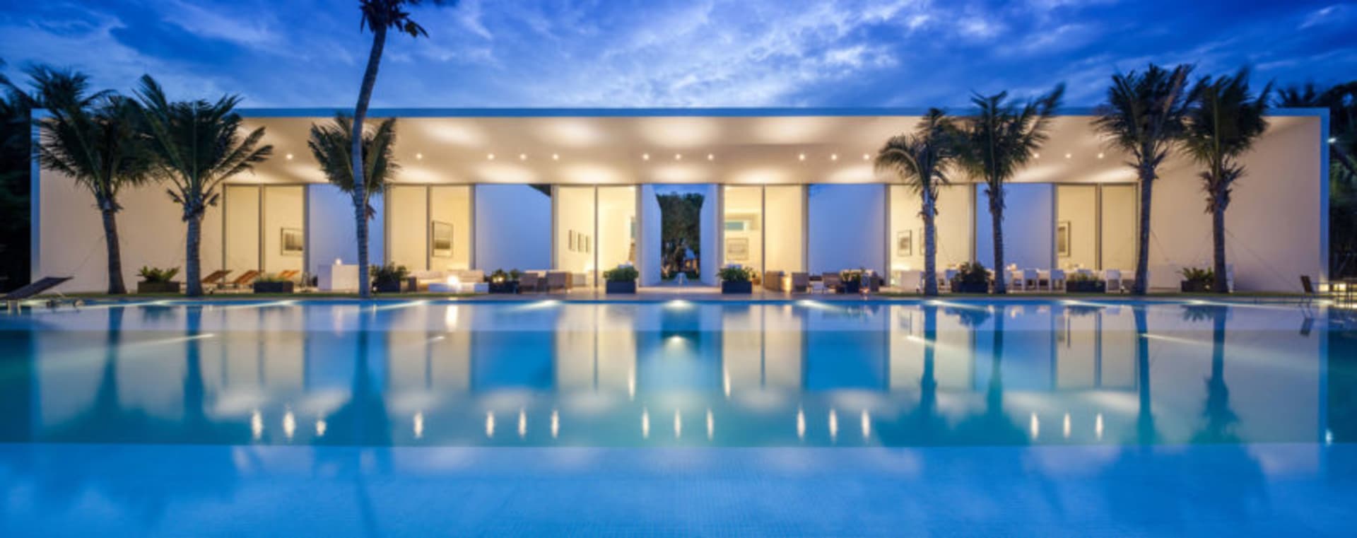 A modern residential pool area with a concrete patio and palm trees.